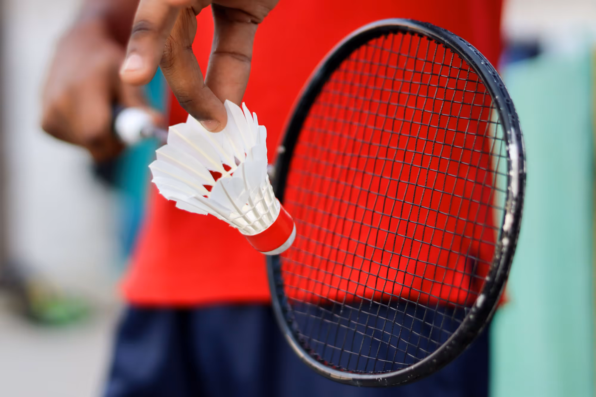 close of someone holding a shuttlecock in front of badminton racket