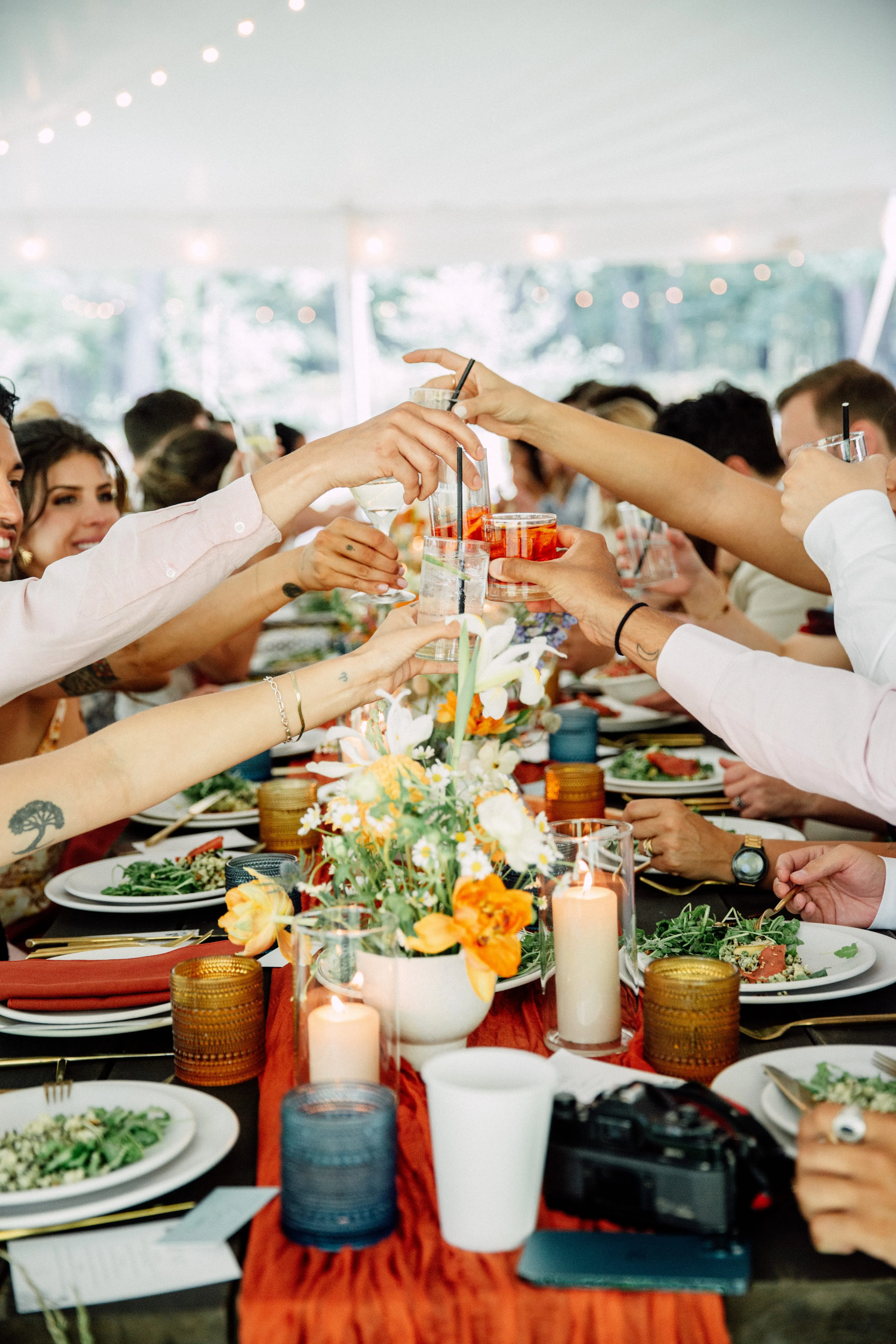 Guests toasting over an orange and white floral centerpiece at a tented Glen Falls House reception