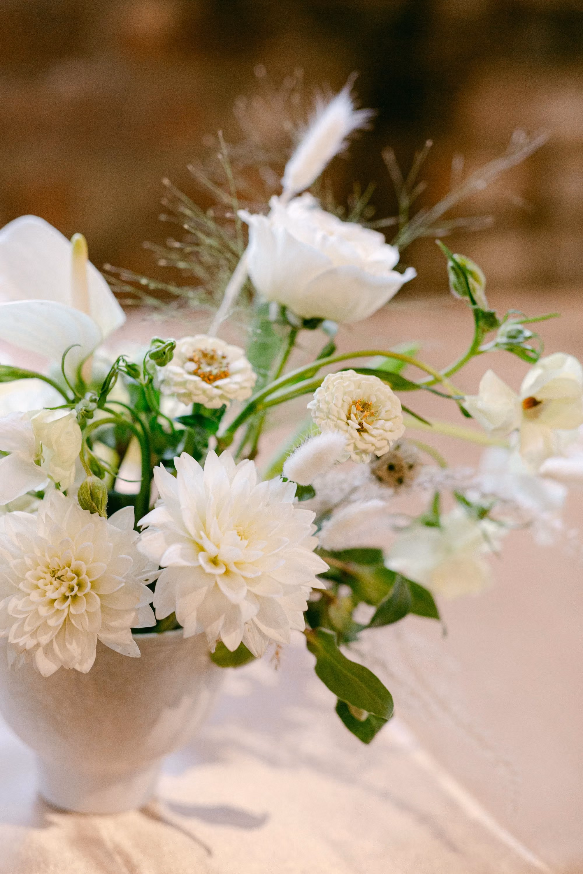 Close-up of a white dahlia, rose, and calla lily arrangement in a ceramic vase.