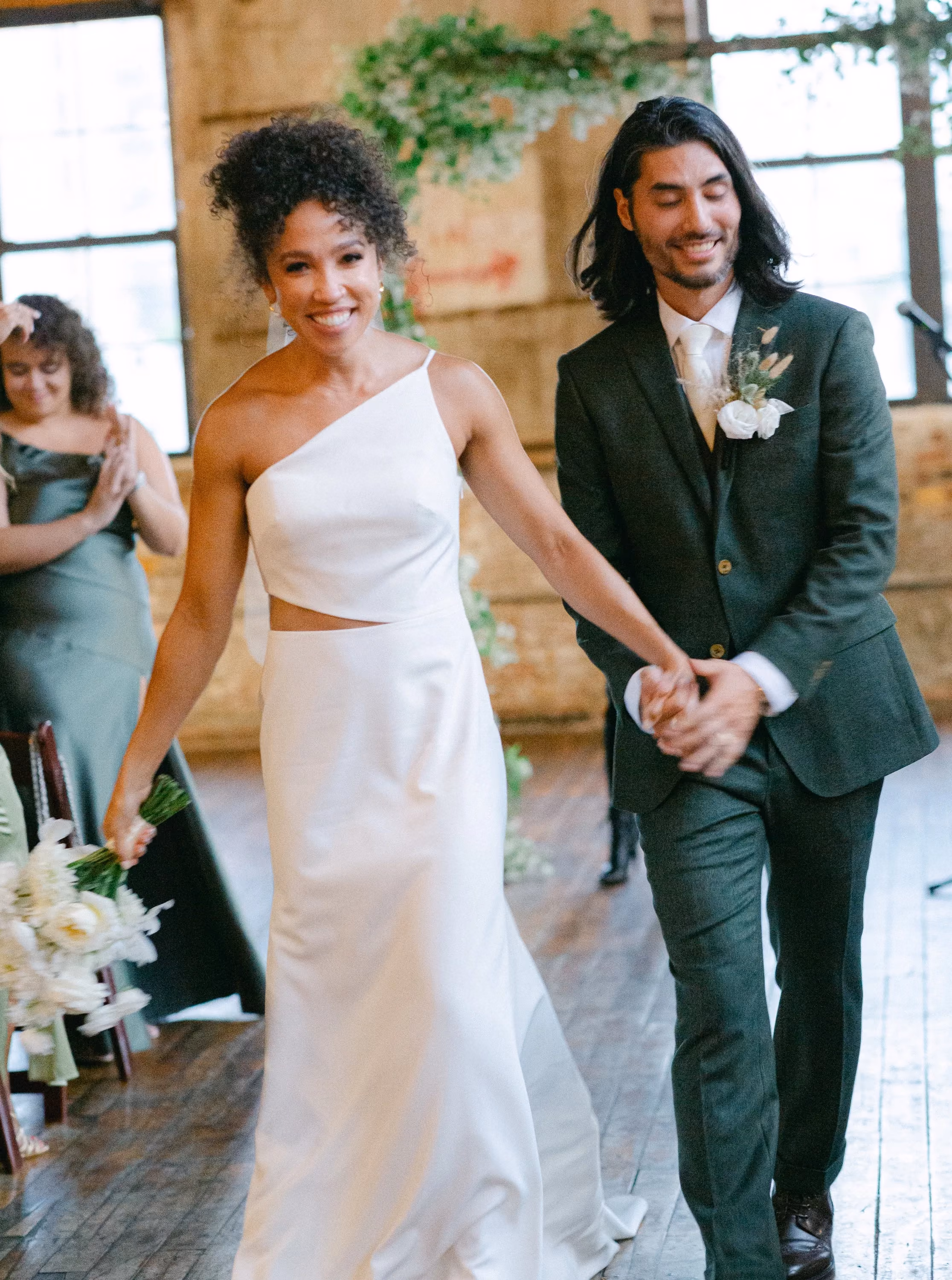 Newlyweds walking hand in hand back up the aisle as guests applaud.