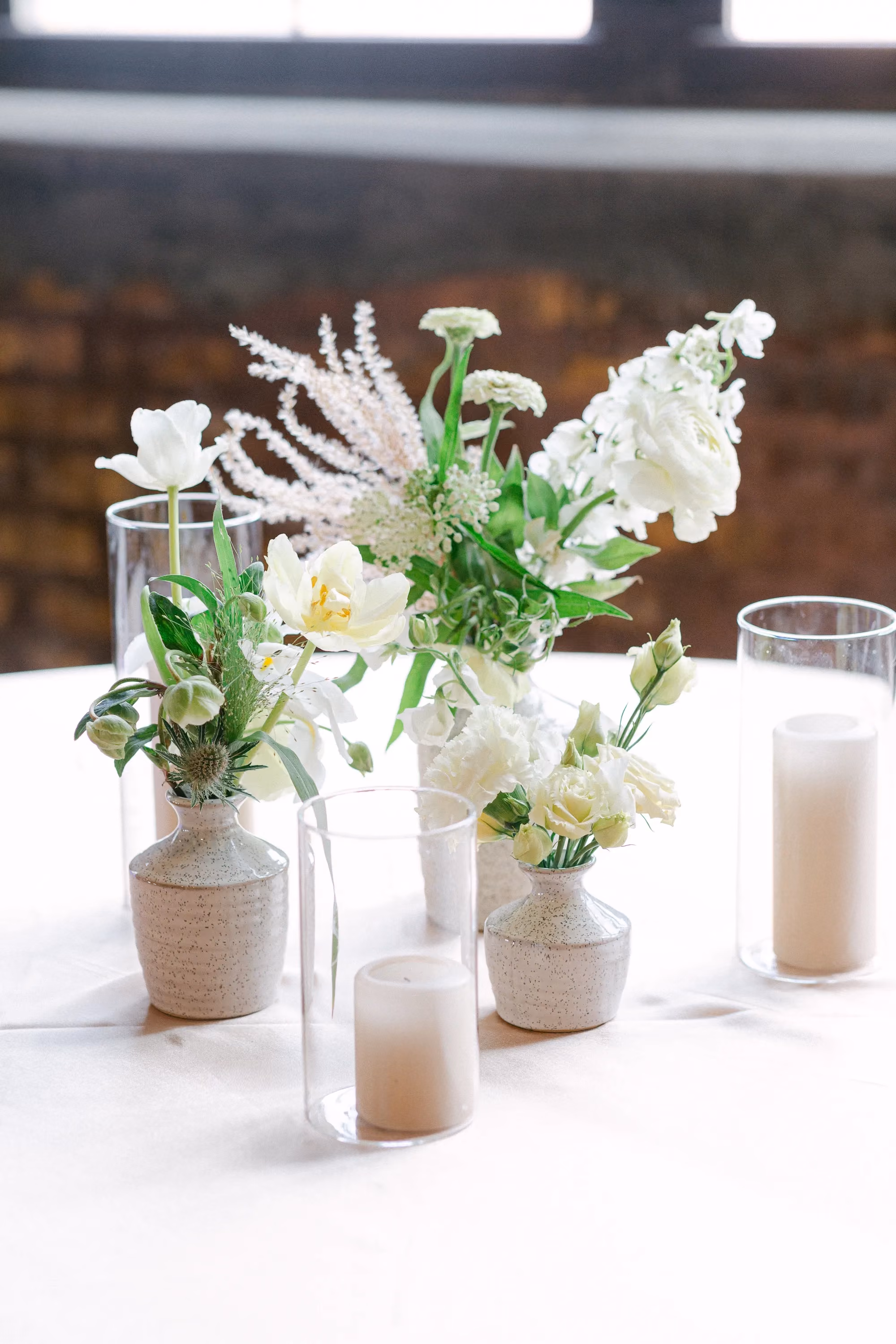 Cluster of bud vases with white tulips and astilbe beside pillar candles on the table.