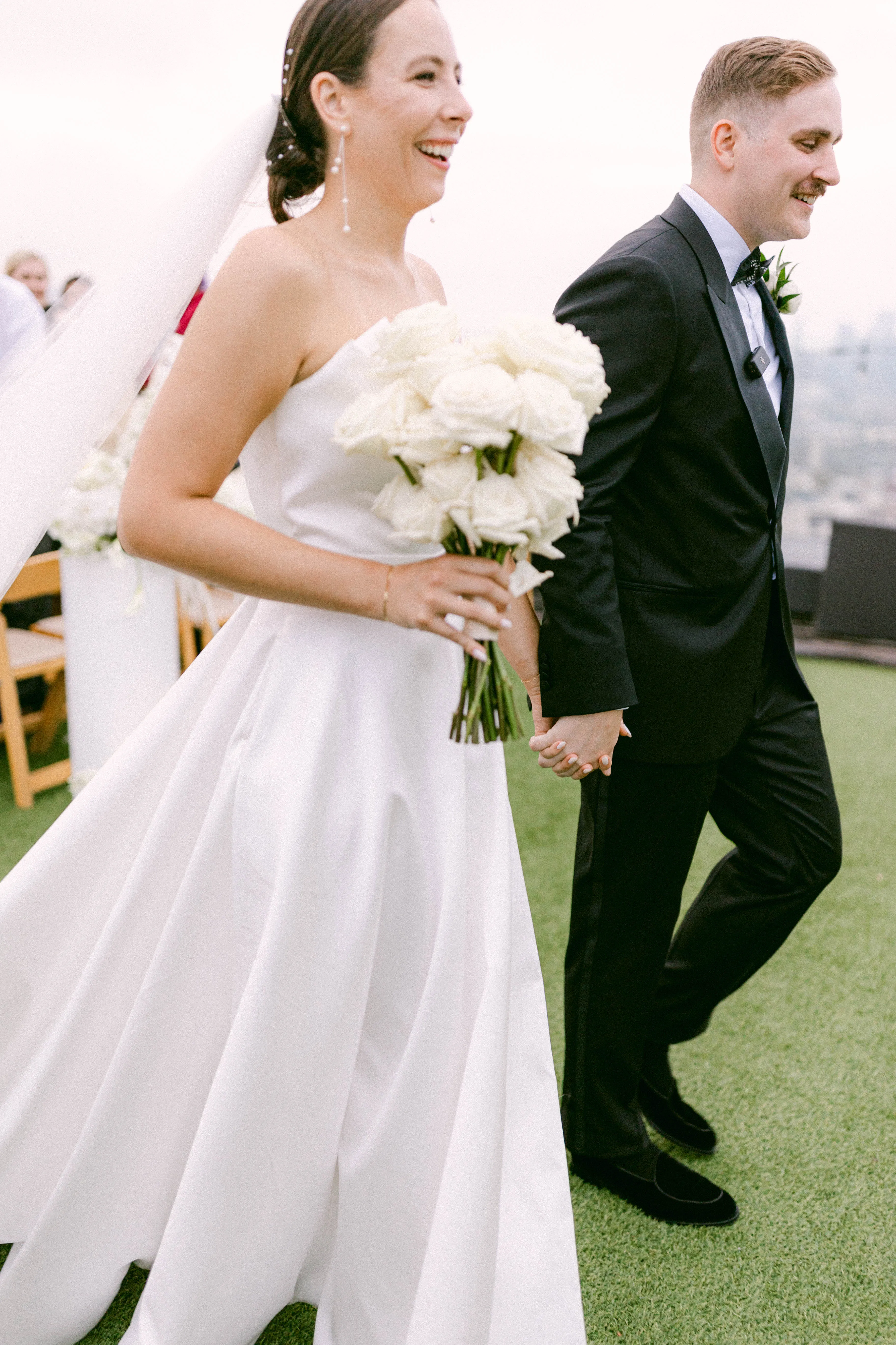 Newlyweds laughing as they walk hand in hand after the rooftop ceremony.