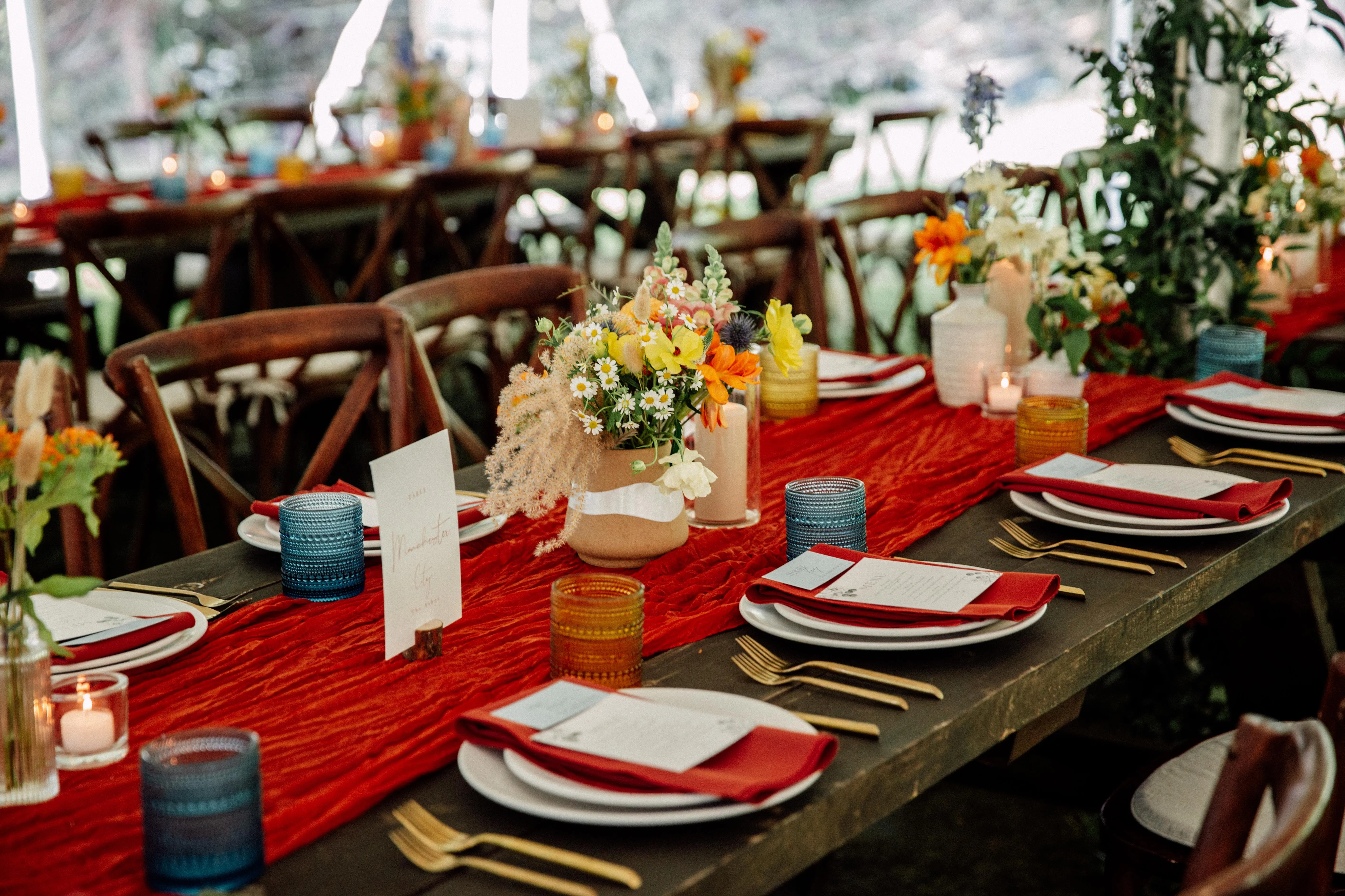 Long reception table with red linen runner, colorful floral centerpieces, and mismatched glassware at Glen Falls House