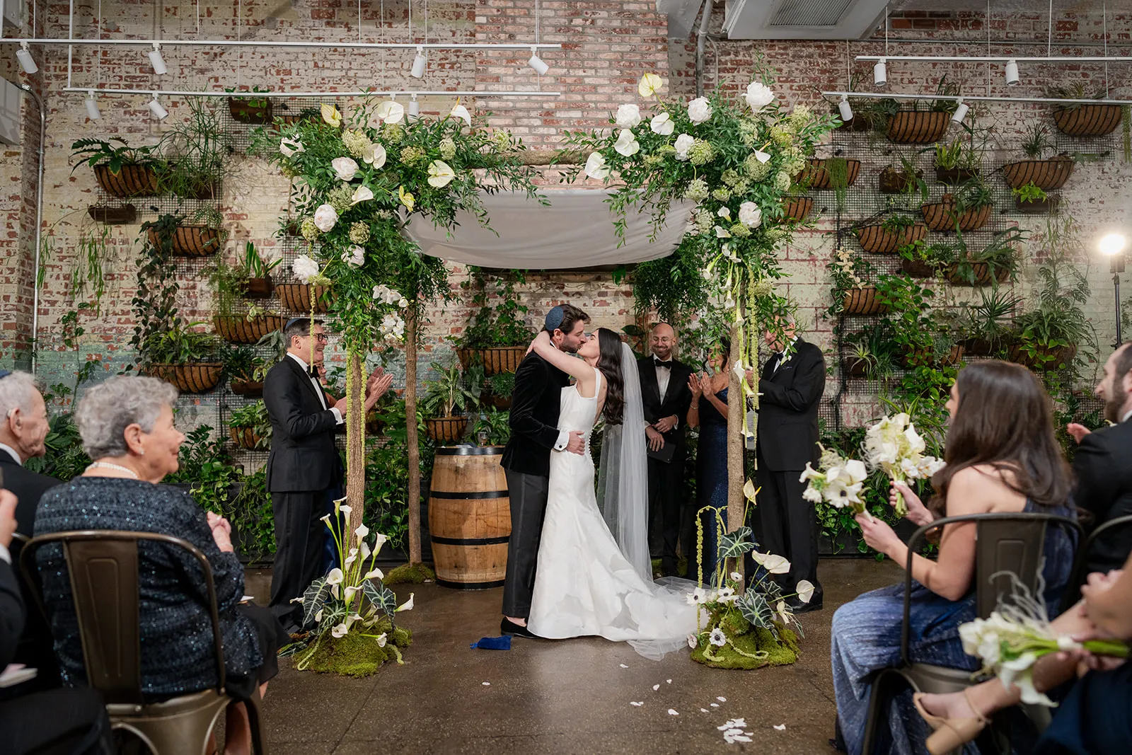 Wedding ceremony under a white floral chuppah at Brooklyn Winery, framed by hanging greenery