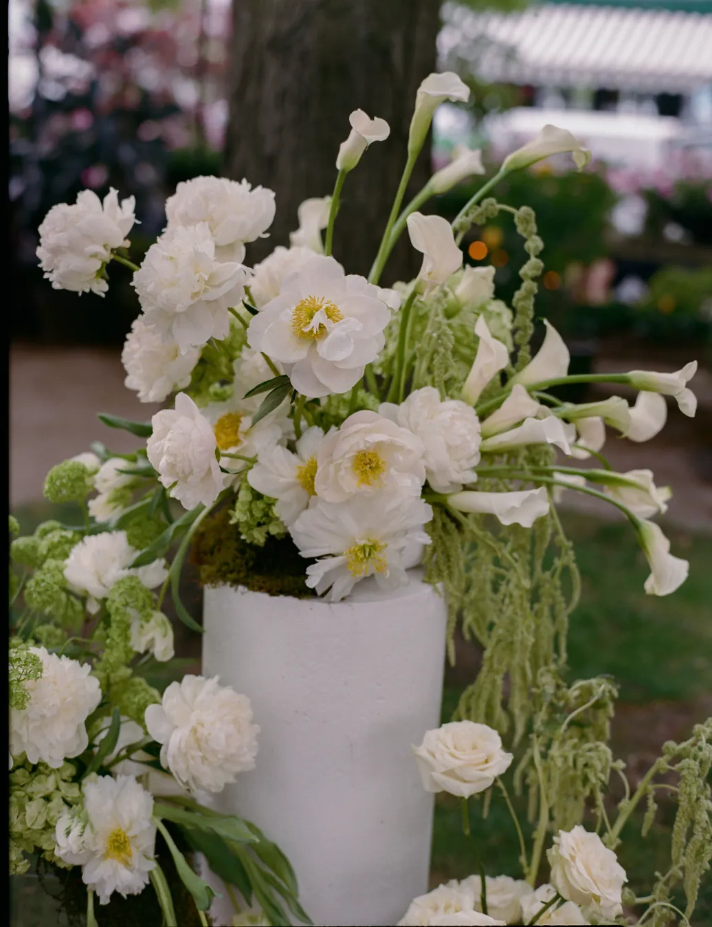 Close-up of white peonies, calla lilies, and green viburnum atop a moss-wrapped pedestal vase