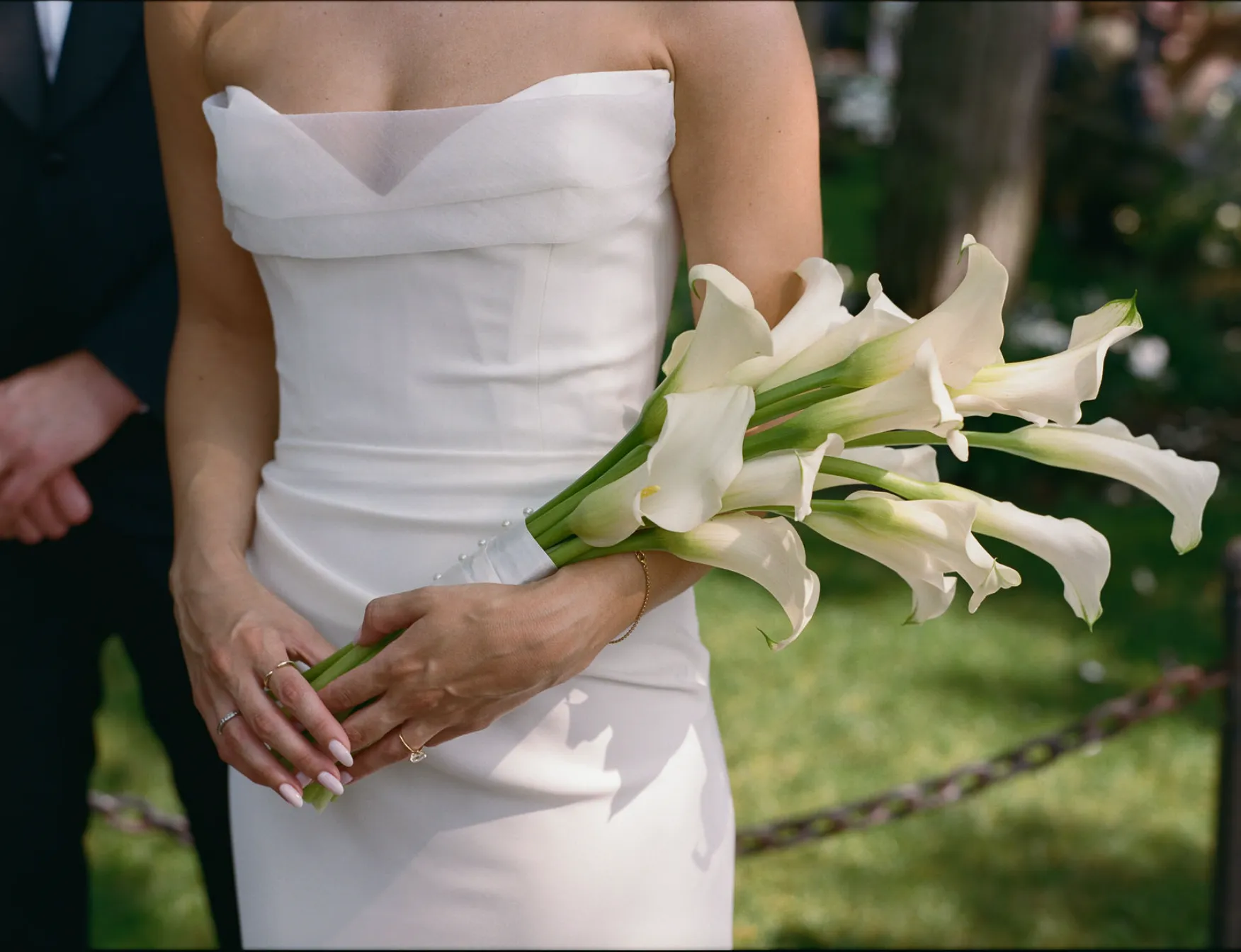 Close-up of bride holding a calla lily bouquet in a fitted white gown beside the groom