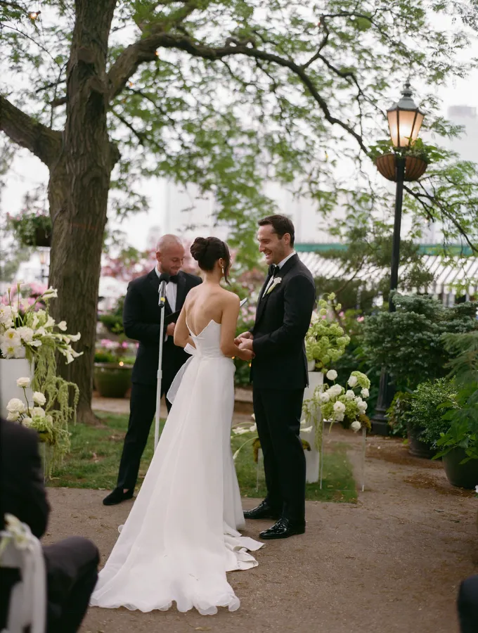 Couple exchanging vows at the altar with the officiant, flanked by white floral arrangements