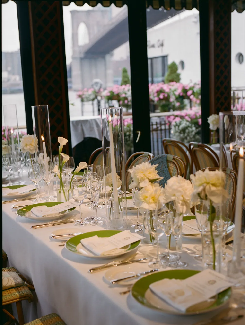 Reception table set with calla lily bud vases and candles, Brooklyn Bridge visible through the windows