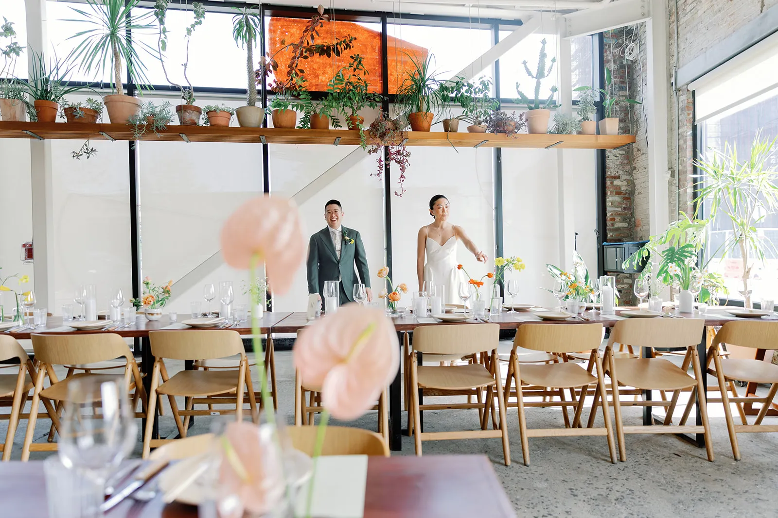 Bride and groom walking through the reception room lined with long tables and blush anthurium centerpieces