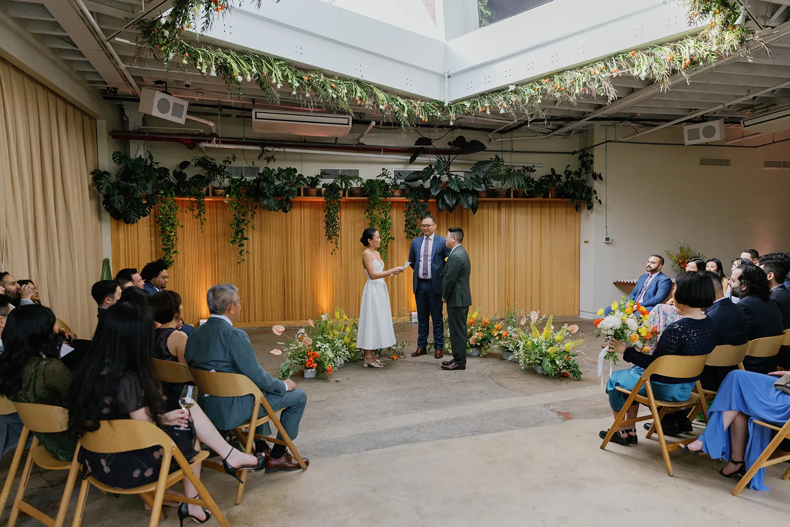 Guests seated for the ceremony beneath the greenery-draped skylight