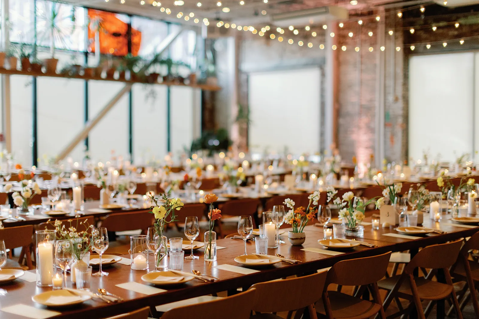 Wide view of the reception room set with long tables, string lights, and candlelit centerpieces