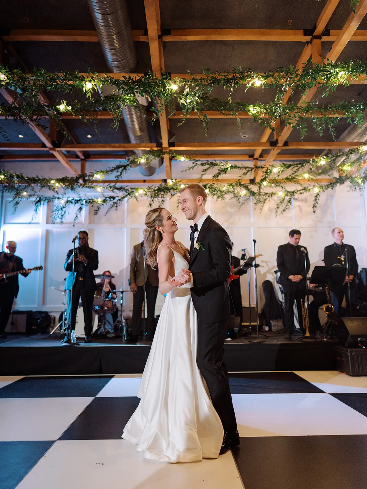 Bride and groom sharing a first dance on a checkered floor with a live band playing
