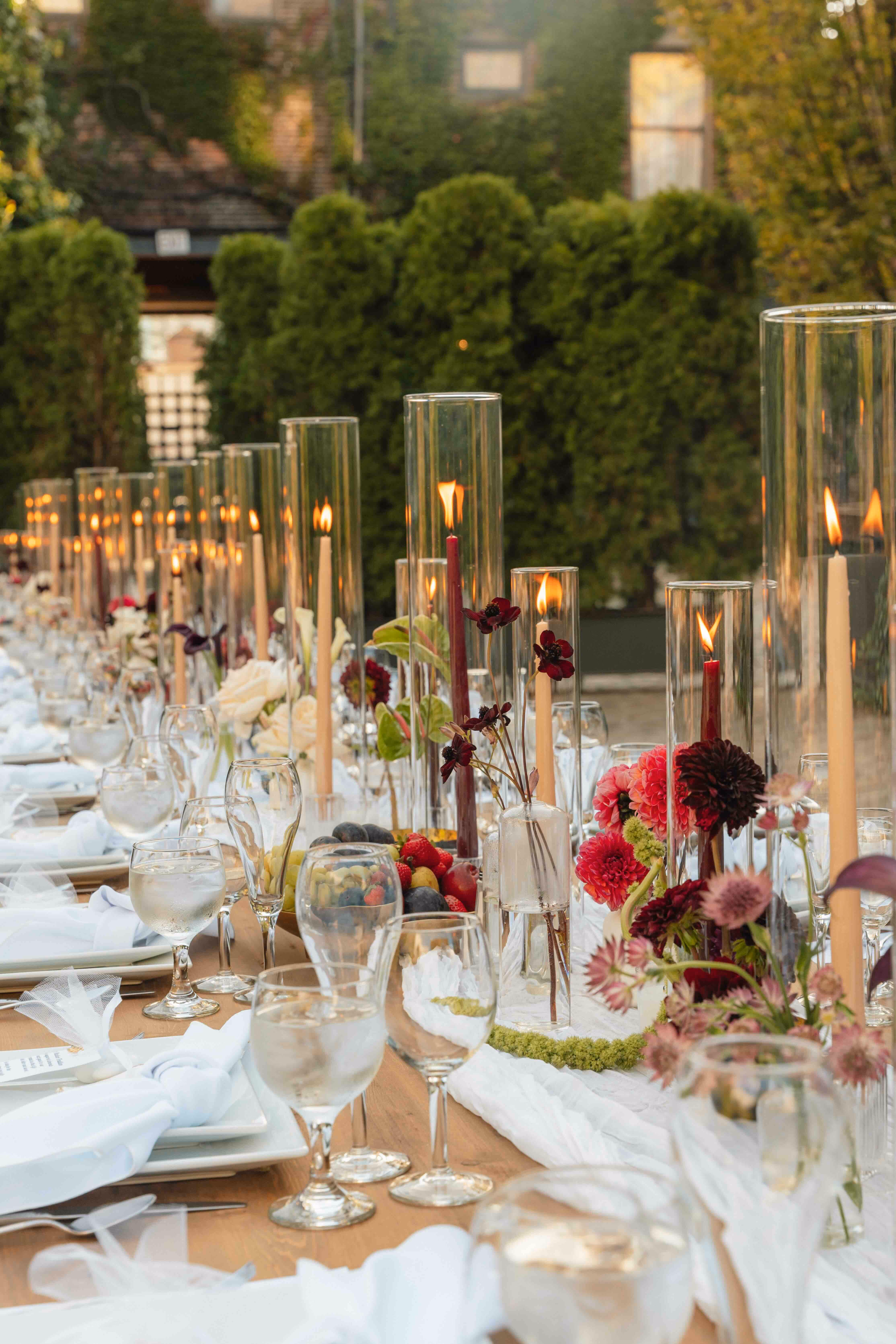 Twilight reception table with tall taper candles in glass hurricanes and burgundy dahlias