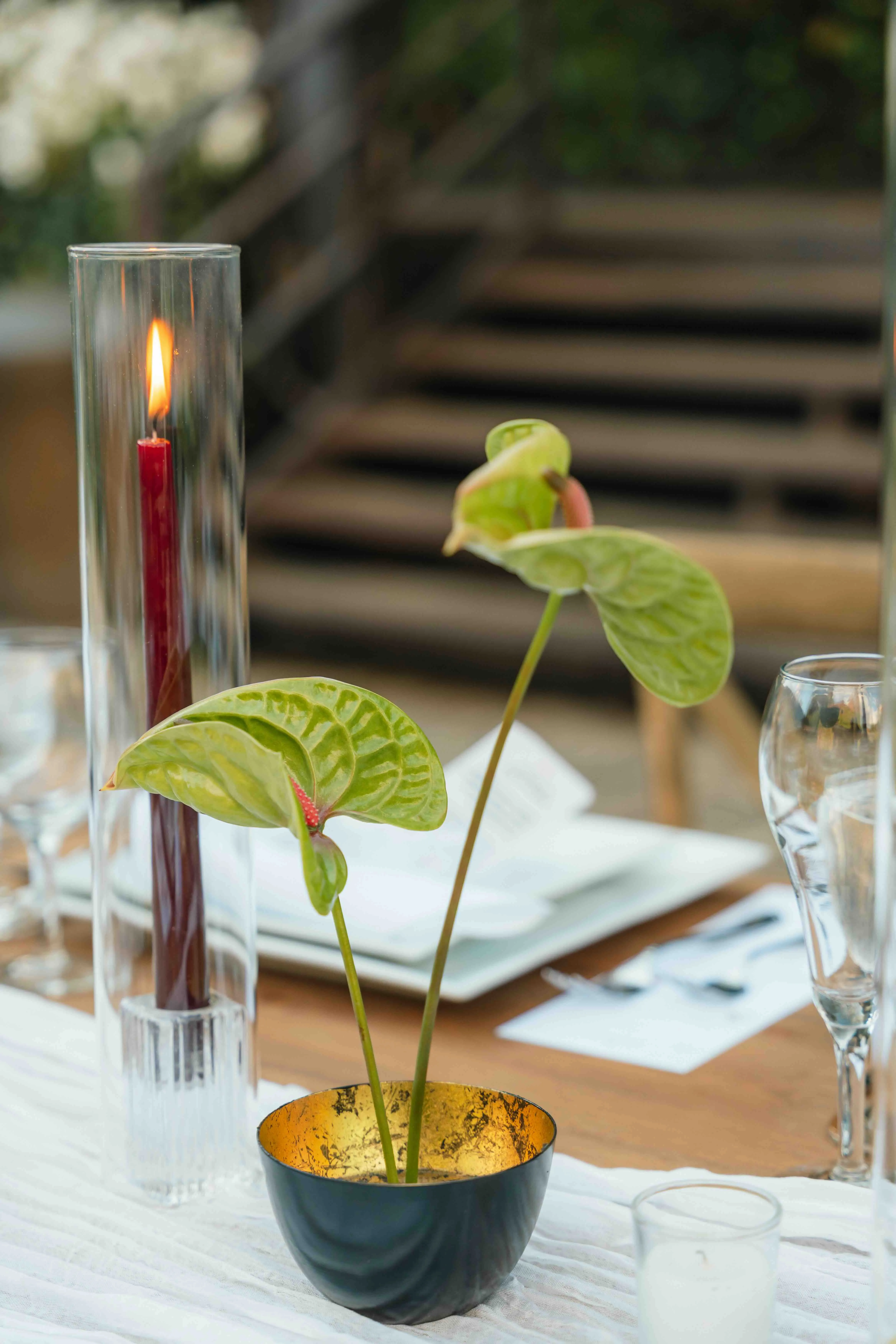 Table detail with green anthurium blooms in a gold-leaf bowl beside a burgundy taper candle