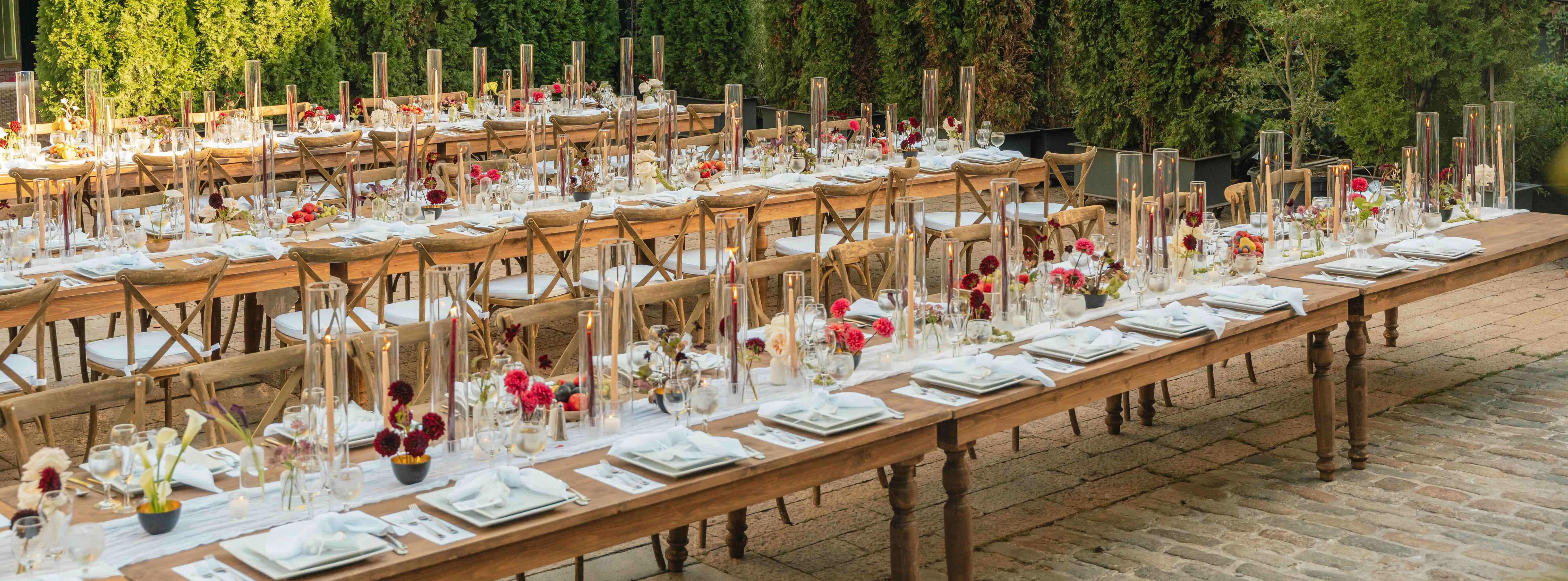 Outdoor reception at The Foundry LIC with a long table set with tall glass candle cylinders and colorful dahlia centerpieces