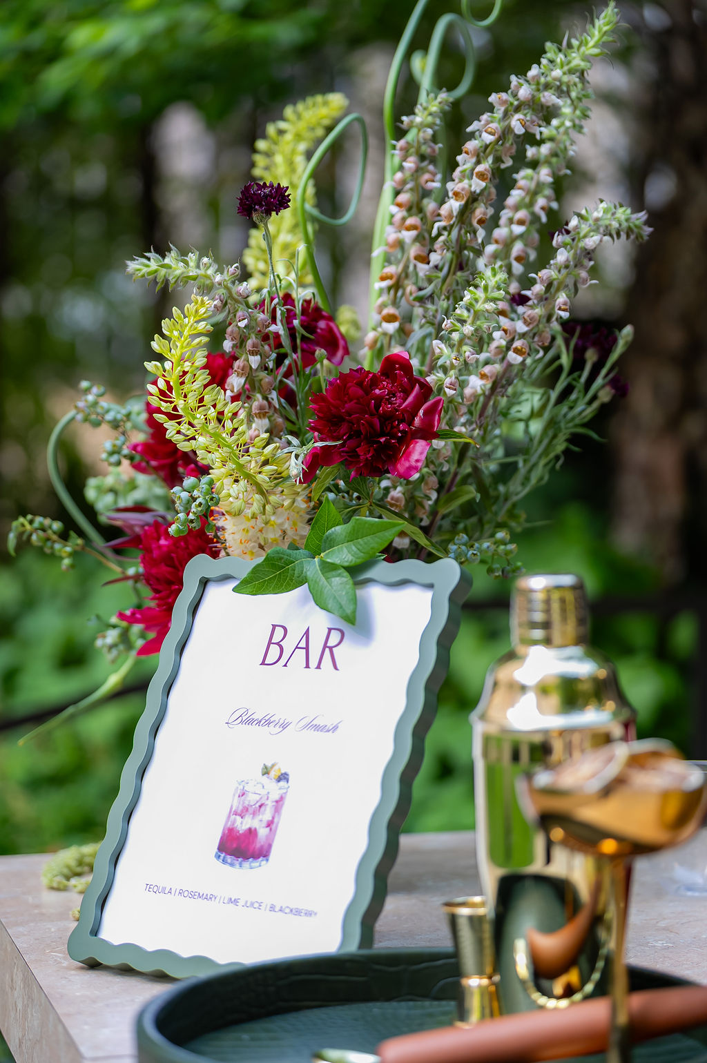 Bar sign styled with a lush red peony and greenery arrangement at an intimate outdoor event