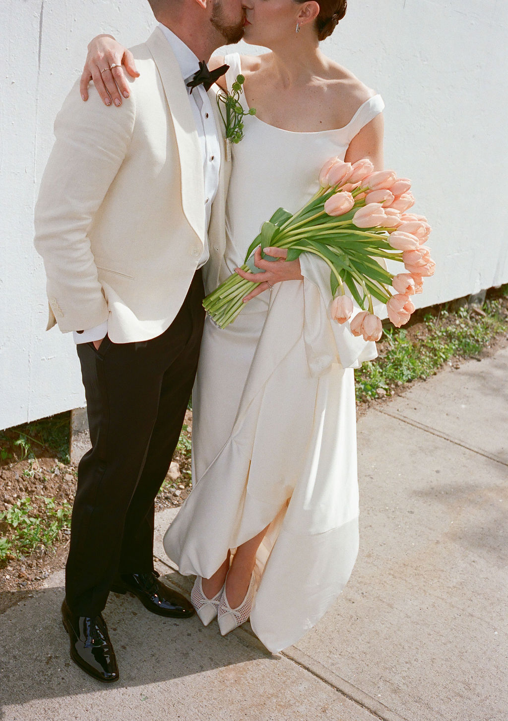 Bride and groom kissing outdoors, bride holding a bouquet of pink tulips