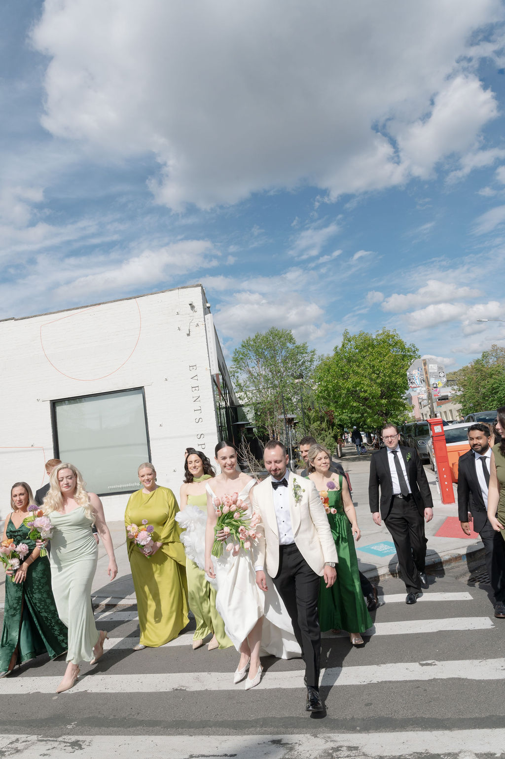 Bride, groom, and wedding party crossing the street outside Rule of Thirds, bride holding pink tulips