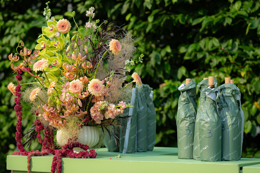Lush arrangement of peach and chartreuse blooms beside wrapped wine bottles on a green table