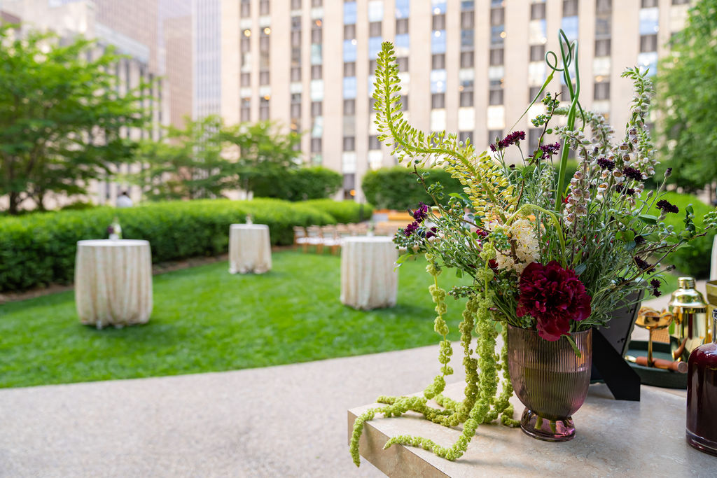 Dramatic floral arrangement with trailing amaranthus and dark red blooms overlooking cocktail tables