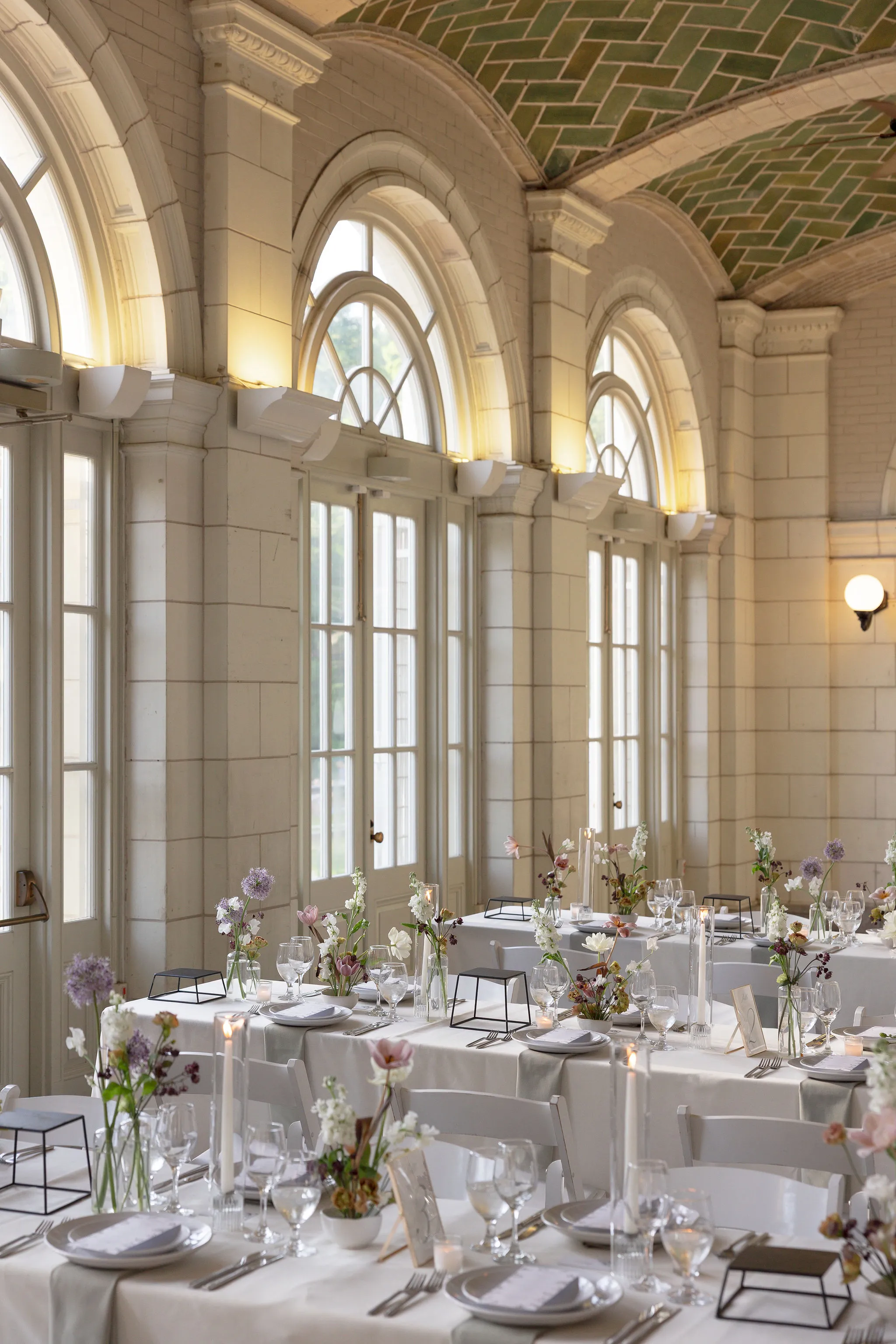 Wide view of the Boathouse reception room's arched windows and vaulted ceiling above tables of bud vase florals.