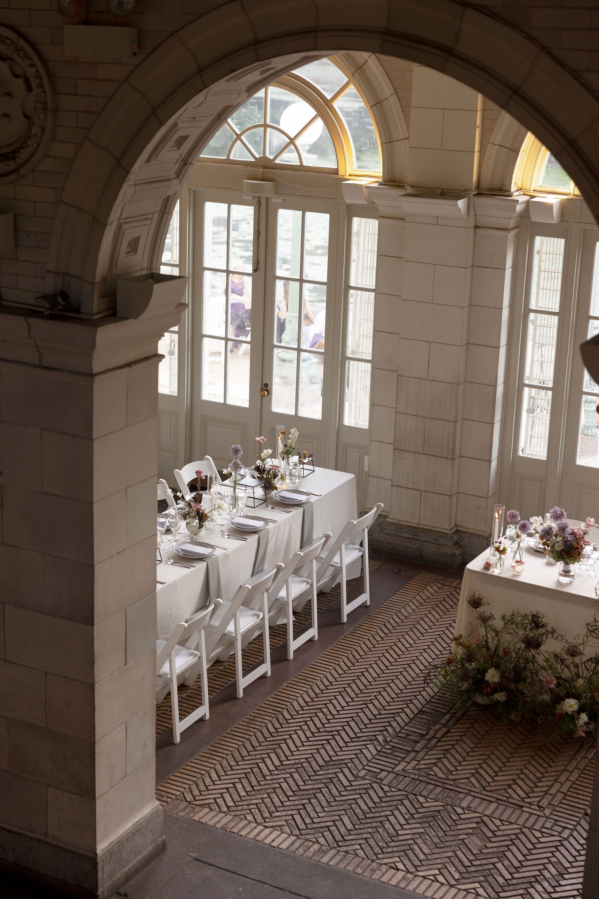 Sunlit Boathouse dining table set with bud vases of allium and seasonal blooms by the windows.