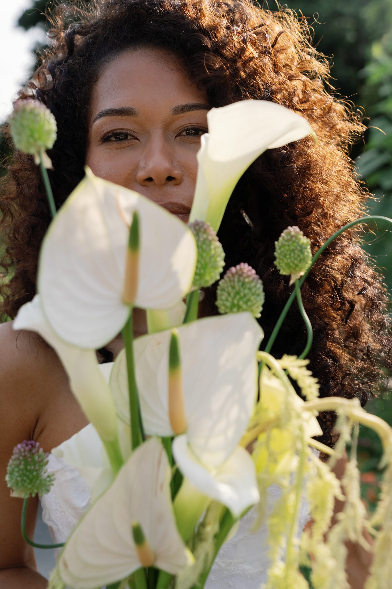 Bride and groom share a kiss on stone garden steps, she holding a textured, modern bridal bouquet with calla lilies, allium and trailing amaranthus.