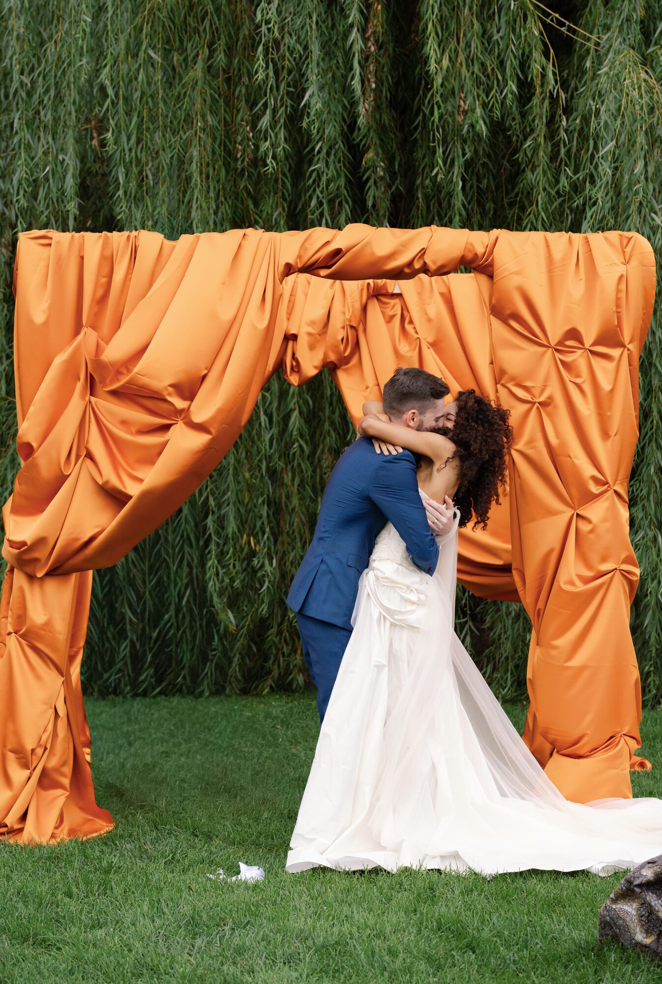 Newlyweds celebrate their recessional, groom cheering with arms raised and bride laughing as they walk away from the orange chuppah.