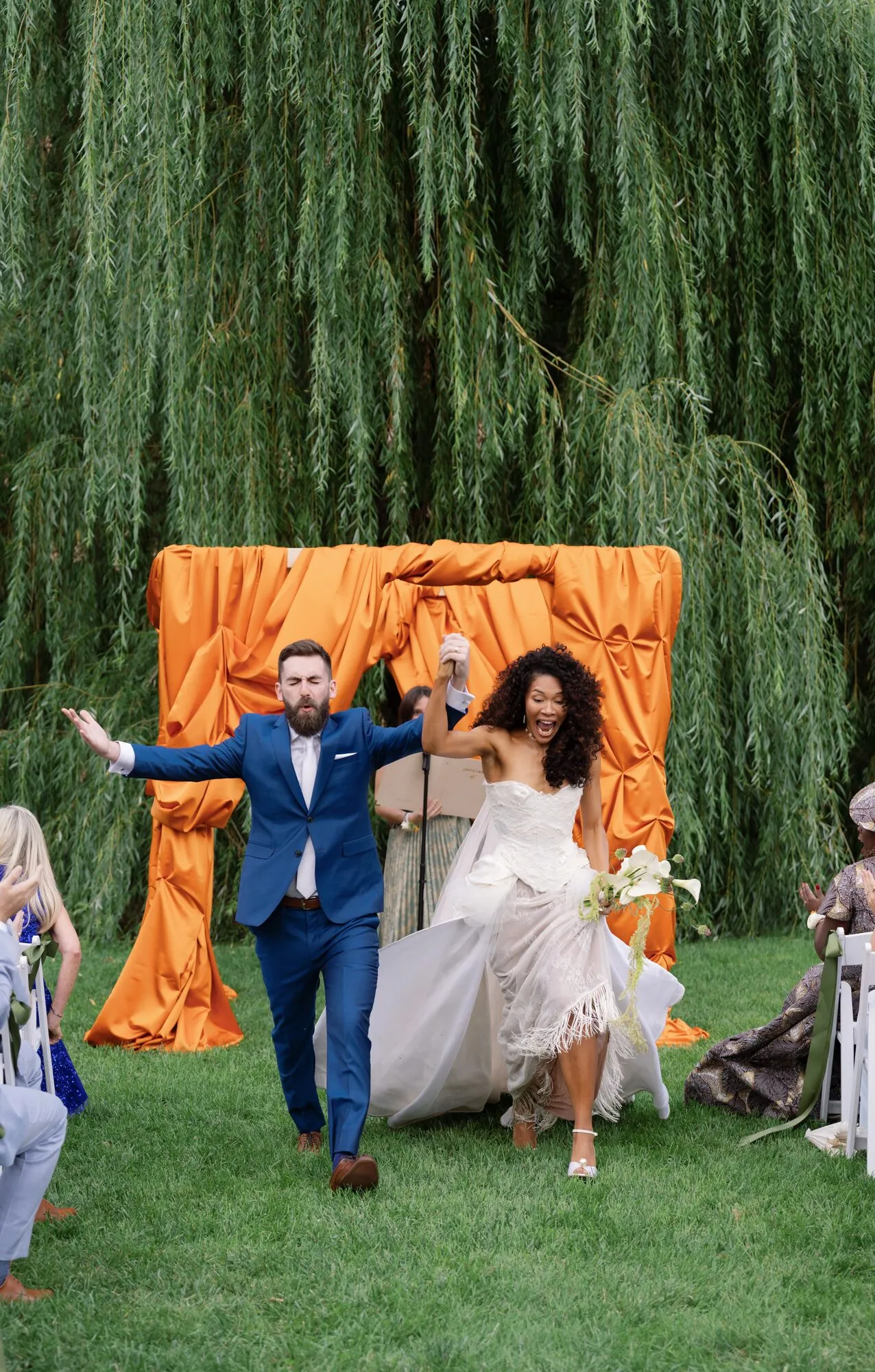 Bride and groom embrace in a kiss beneath the orange-draped chuppah just after their ceremony.