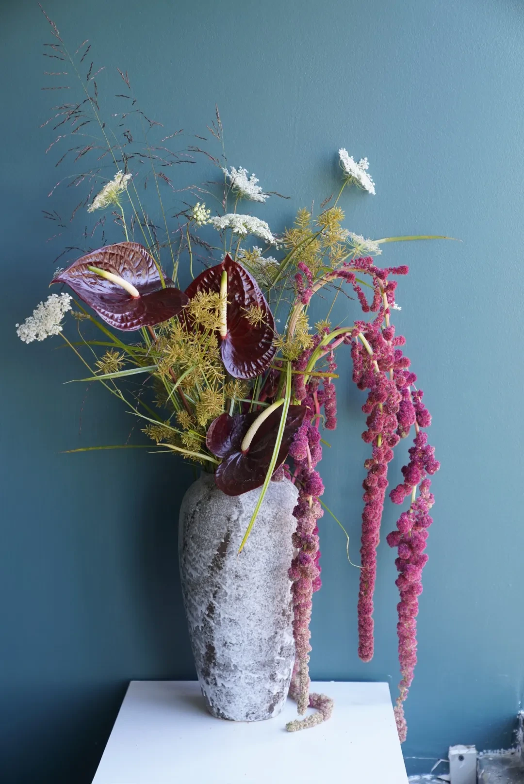 Dark burgundy anthurium with trailing amaranthus and queen anne's lace in a stone vase
