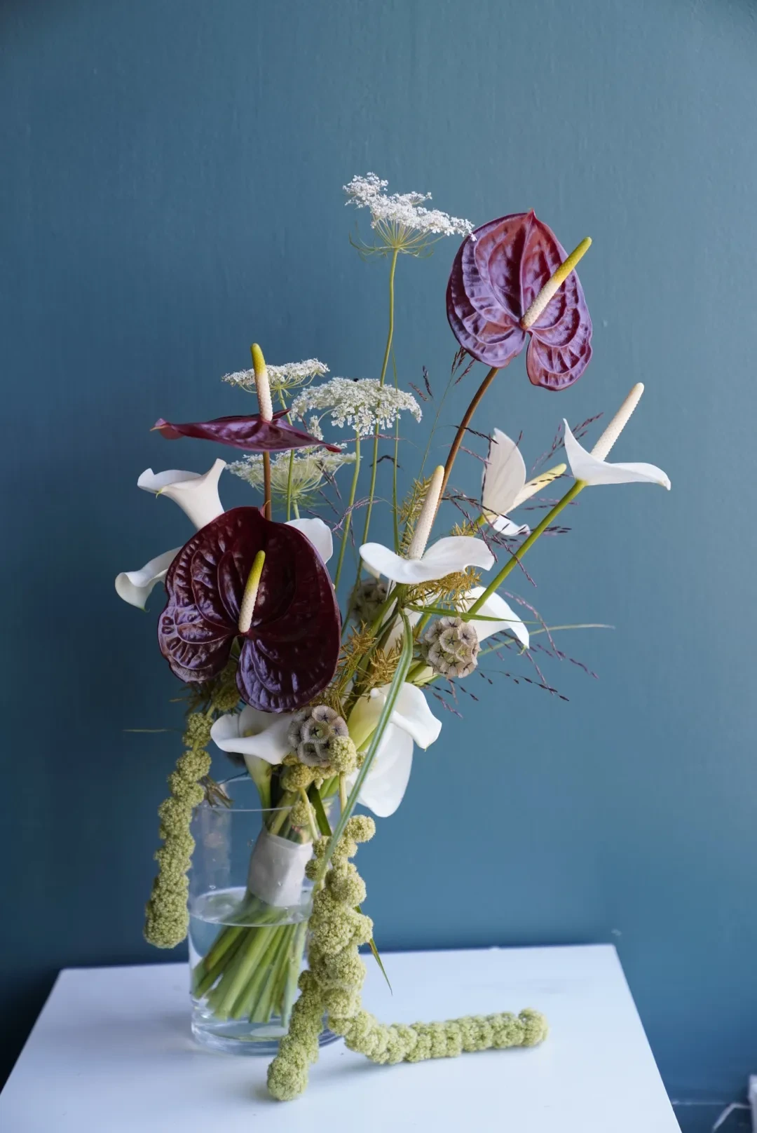 White and burgundy anthurium with trailing green amaranthus in a stone vase