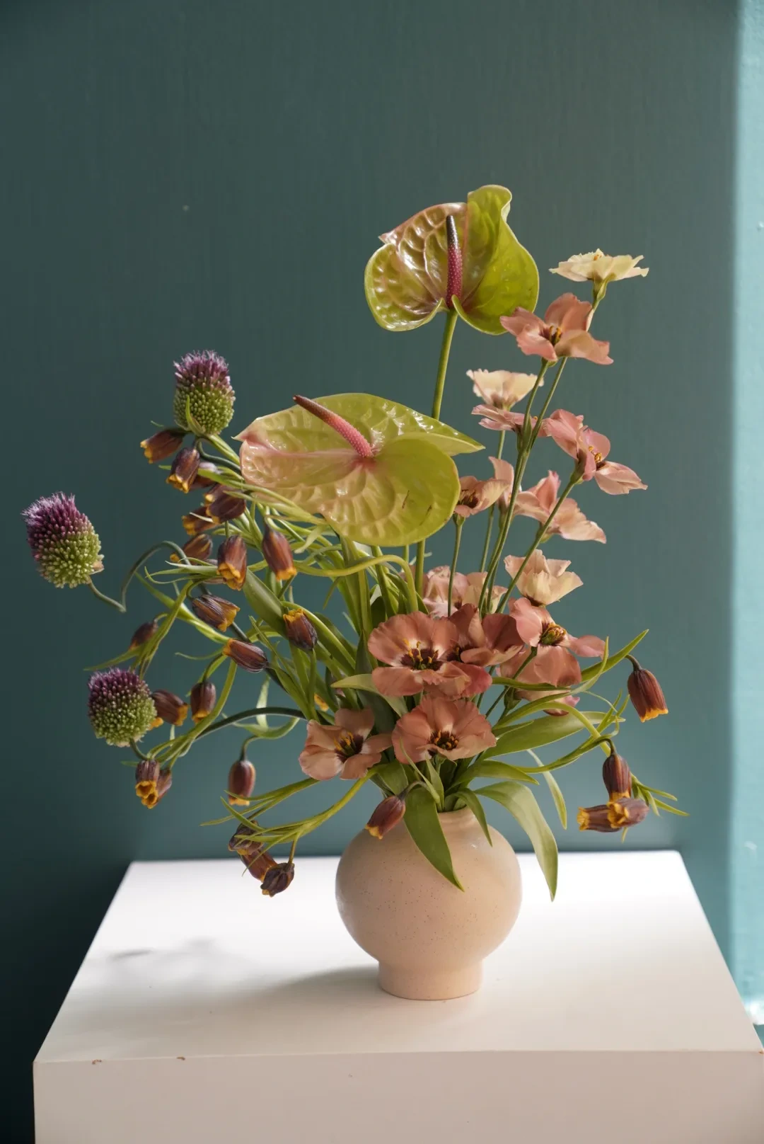 Green anthurium, purple scabiosa and coral bell-shaped blooms in a white vase
