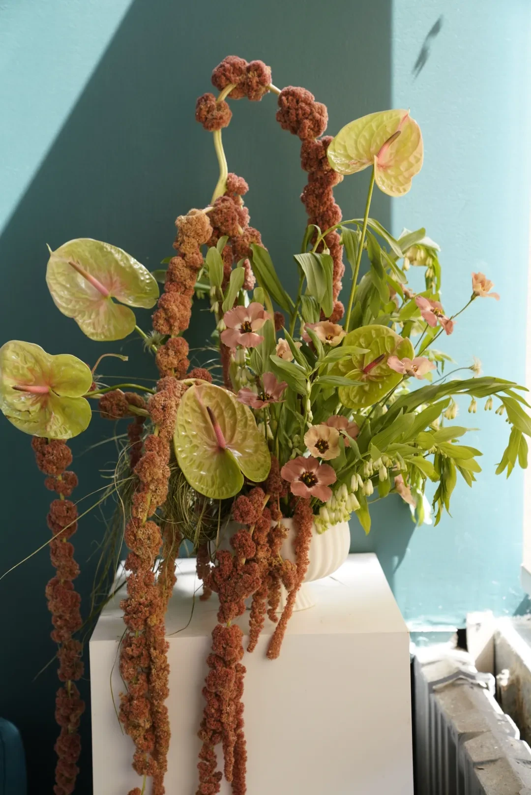 Green anthurium with trailing rust amaranthus and coral blossoms in a white vase