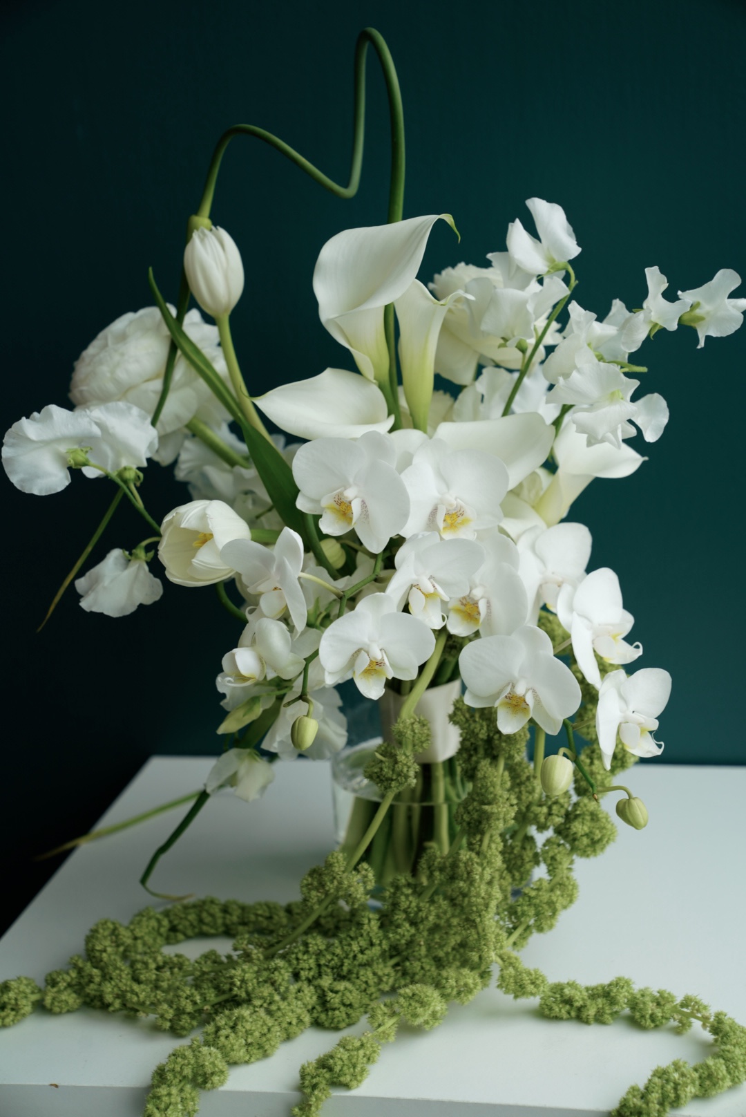 Pink cherry blossom branches in a glass vase against a teal wall
