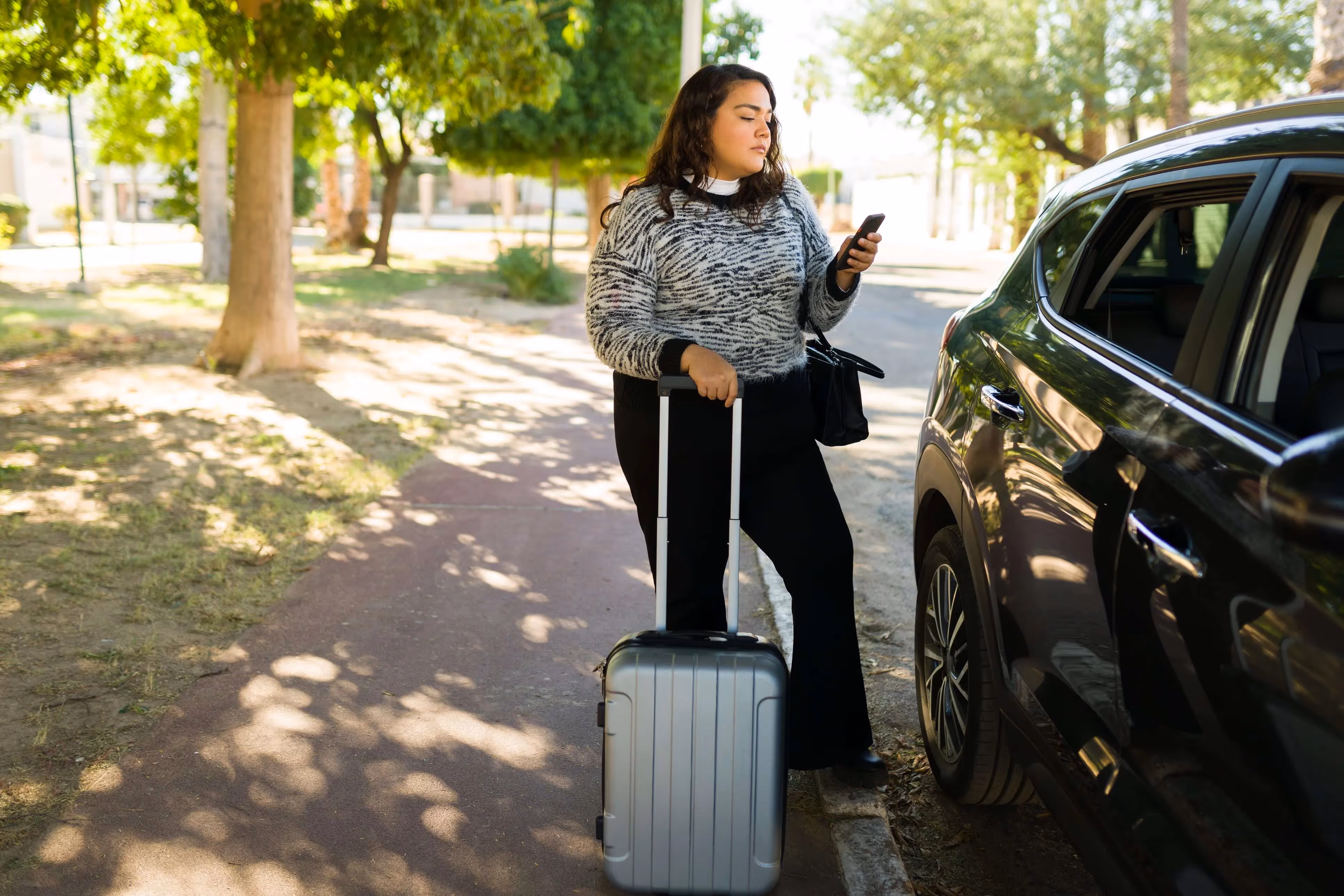 A woman standing with her suitcase and reading about Uber sexual assault on her phone.