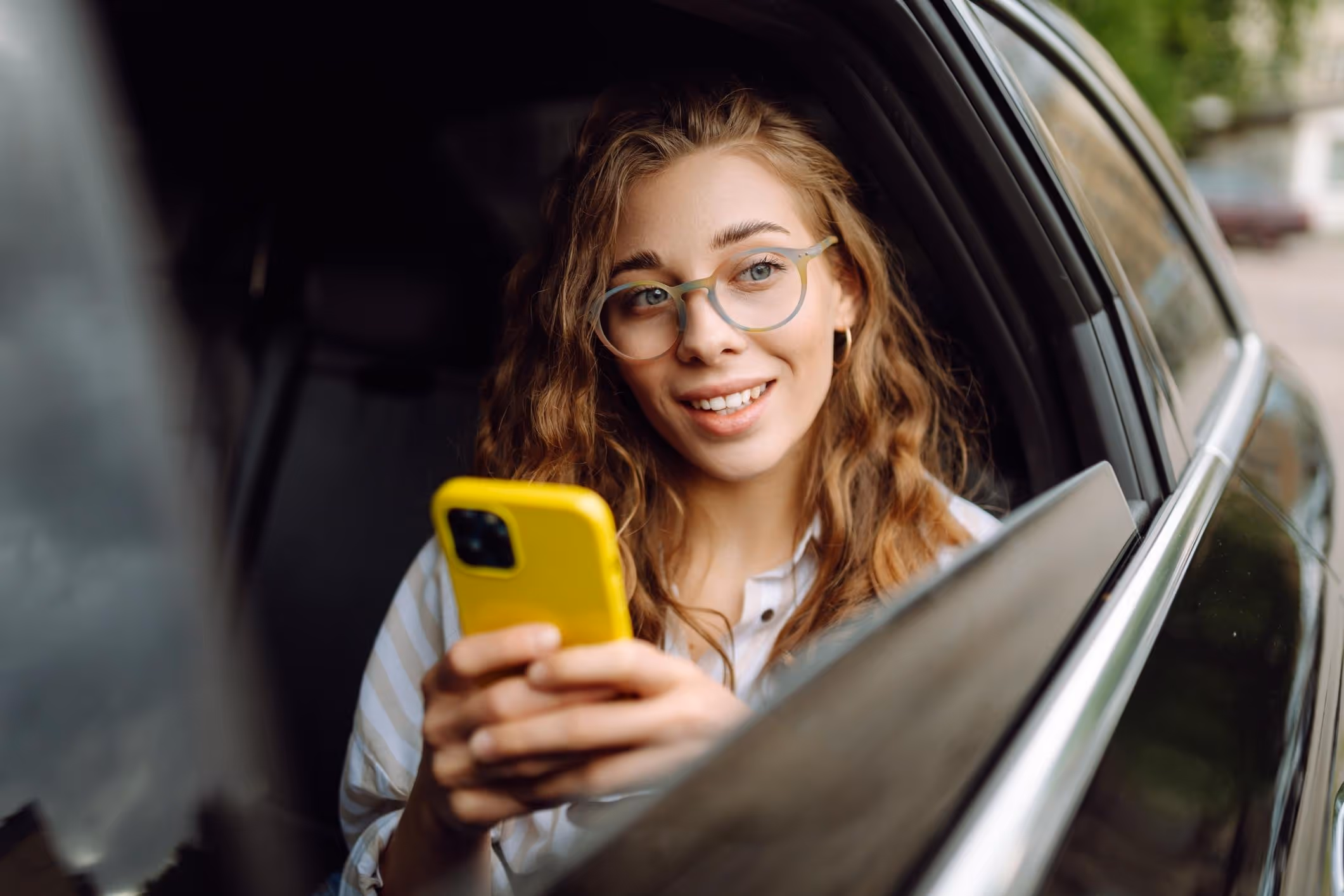 Young woman in back seat of rideshare car using phone, referencing Uber safety tools.
