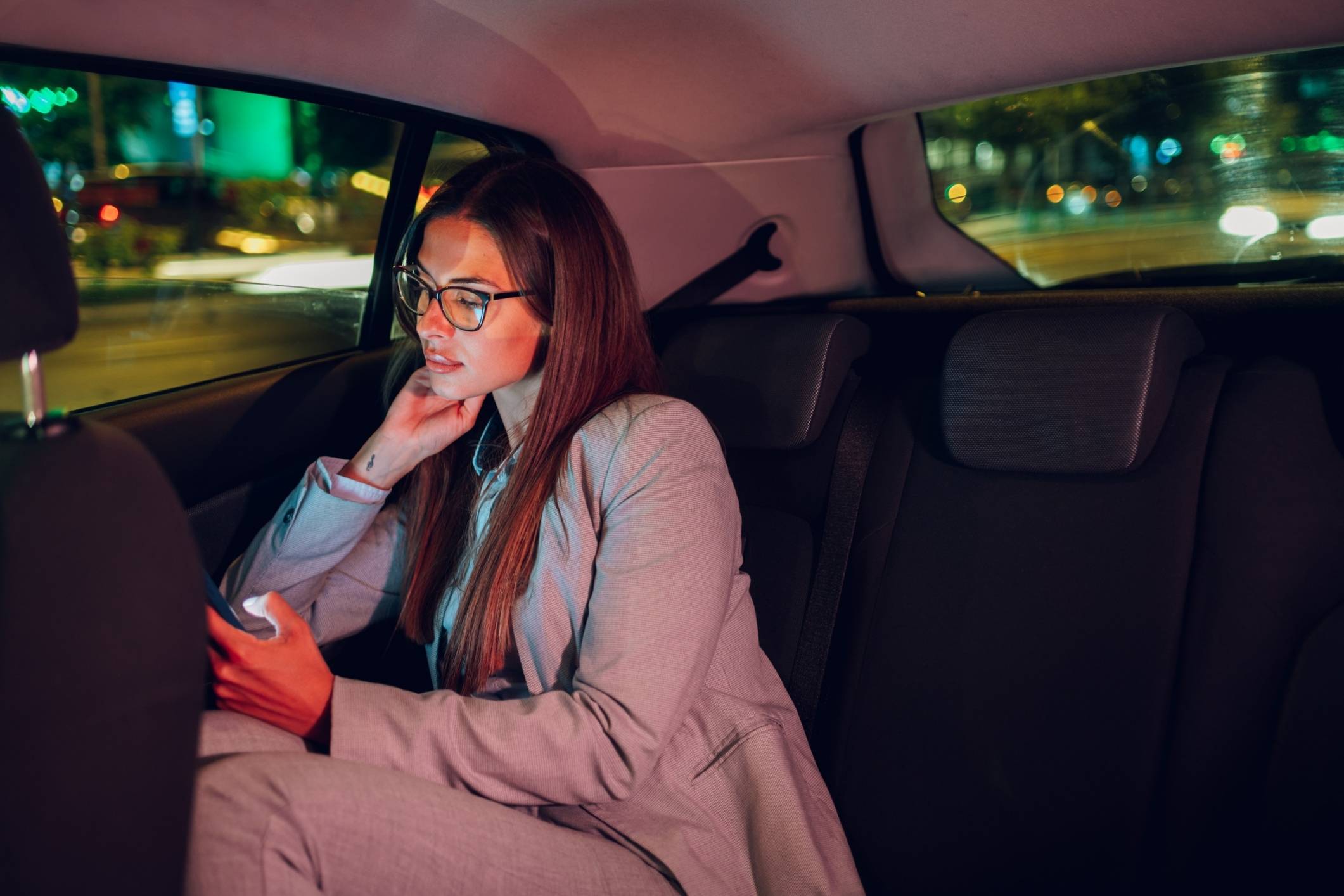 Woman in backseat of car at night using her phone, reflecting need for a San Diego Uber sexual assault lawyer.