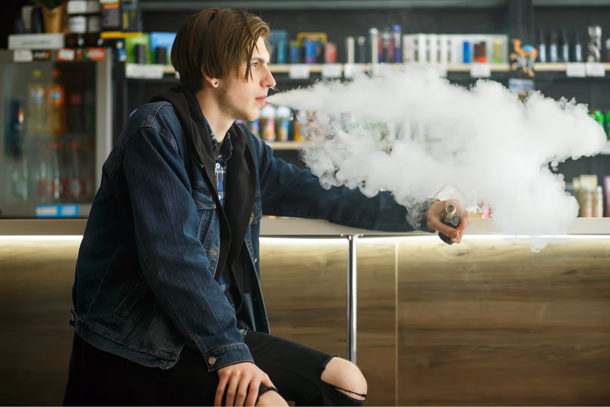 A young man in a black jacket smoking an electronic cigarette in the vape bar