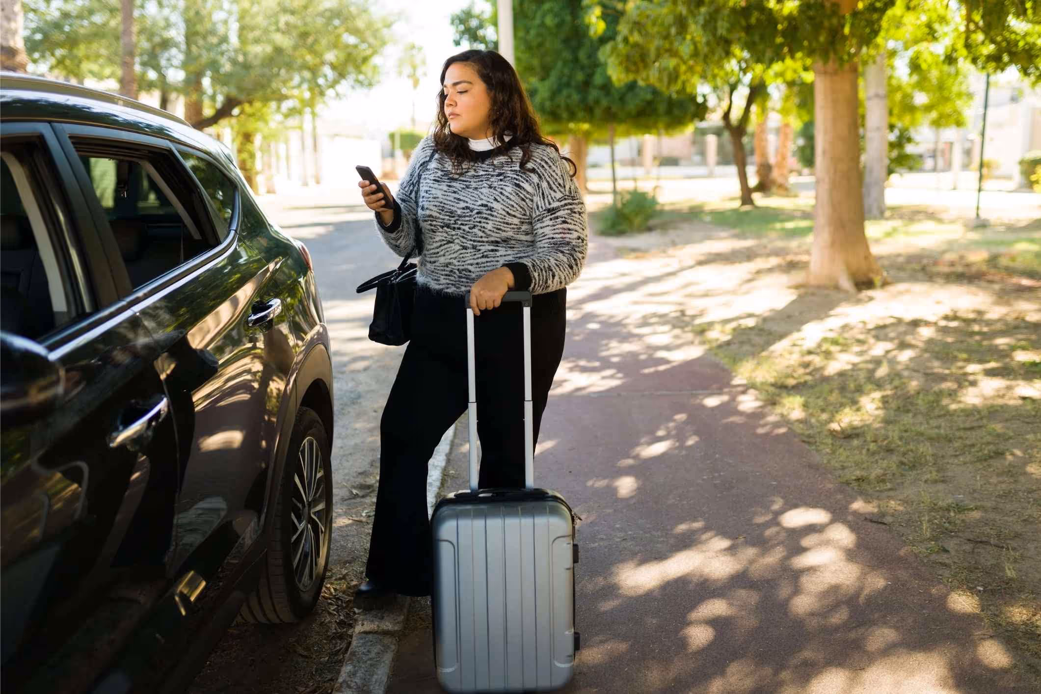 A woman standing with her suitcase and reading about Uber sexual assault on her phone.