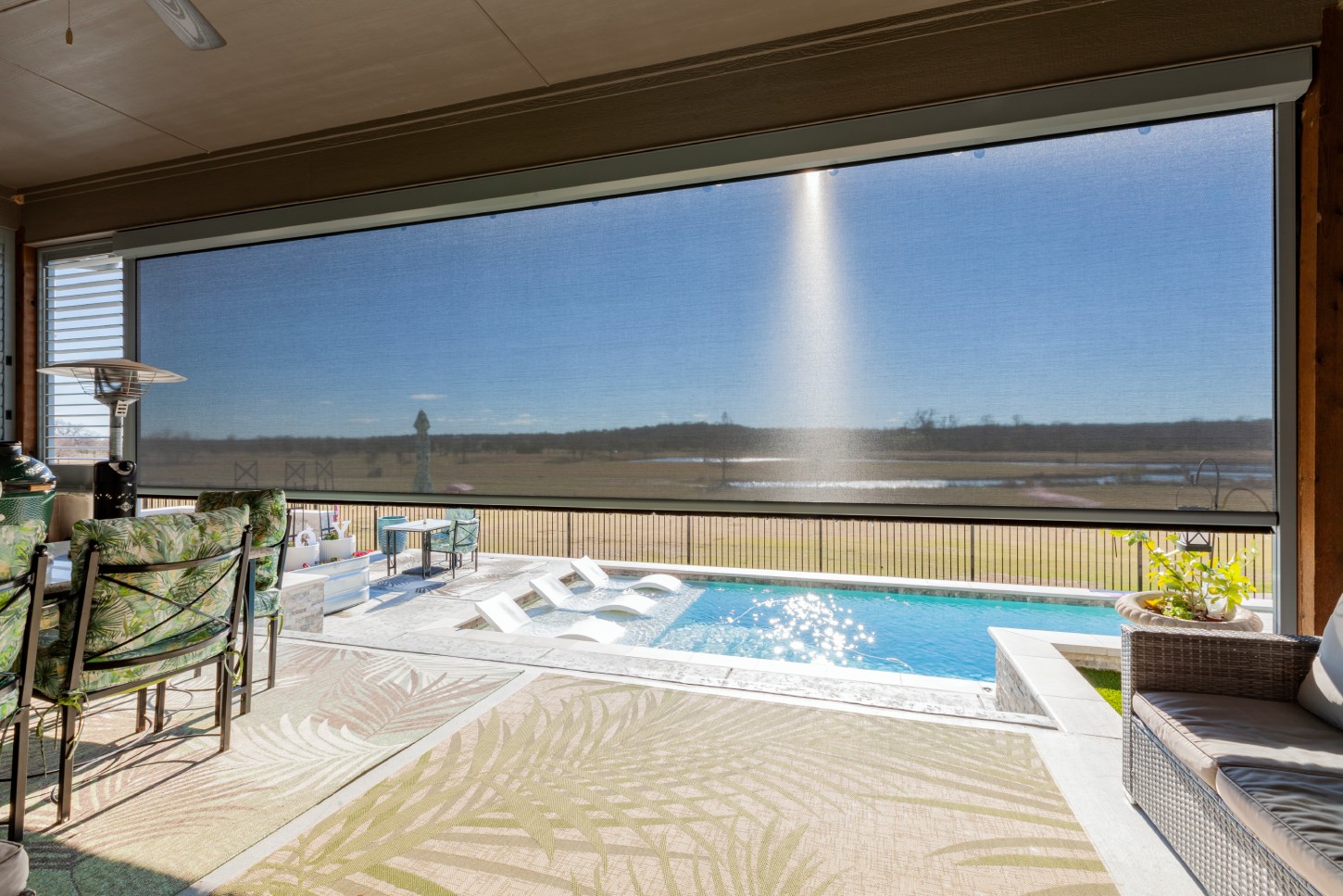 Poolside patio with sun shade overlooking field.