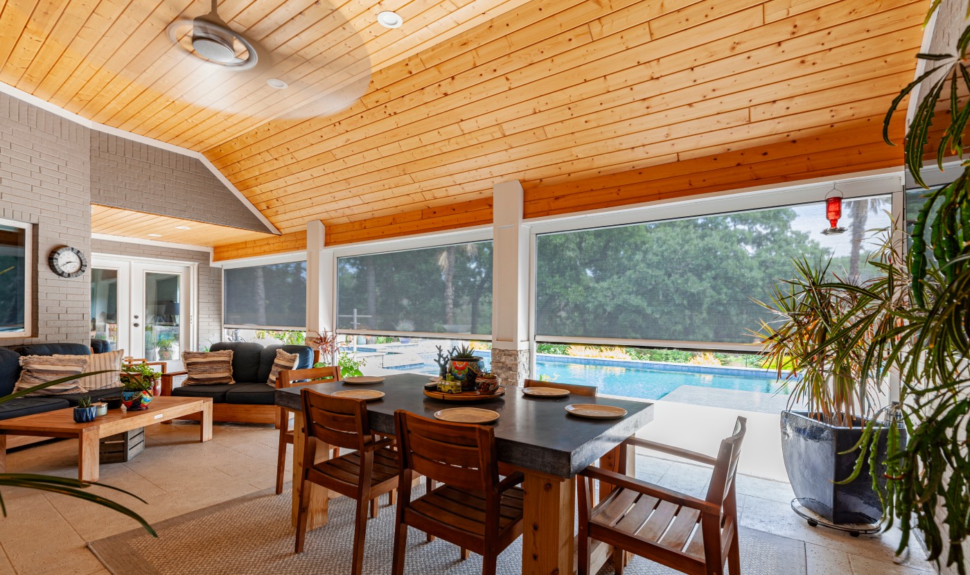 Outdoor patio with screen shades, wooden ceiling, dining table, and pool view.