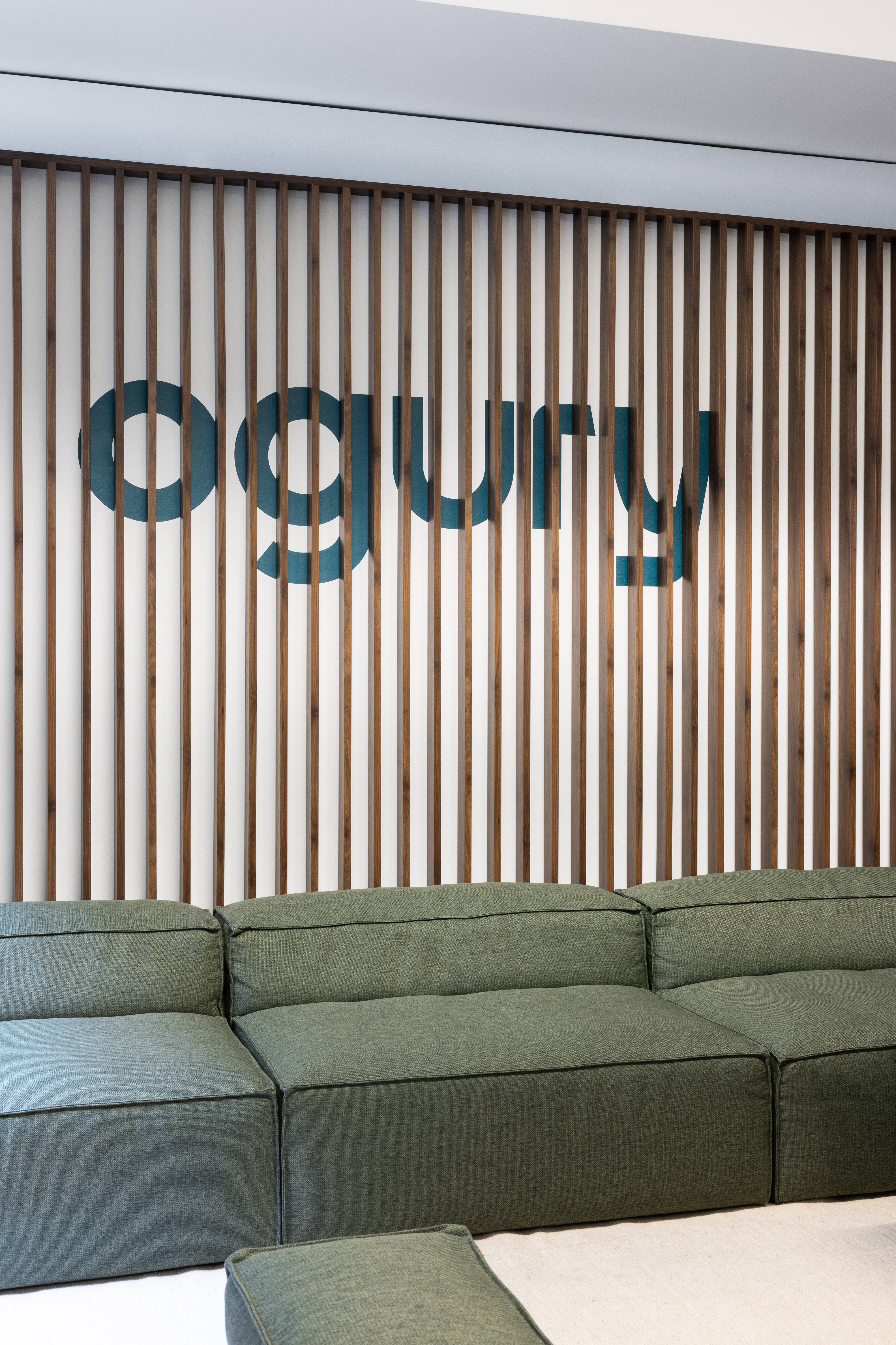 Mur d’accueil Ogury Milan avec logo découpé sur lames de bois verticales et canapé vert, design intérieur réalisé par Slean.