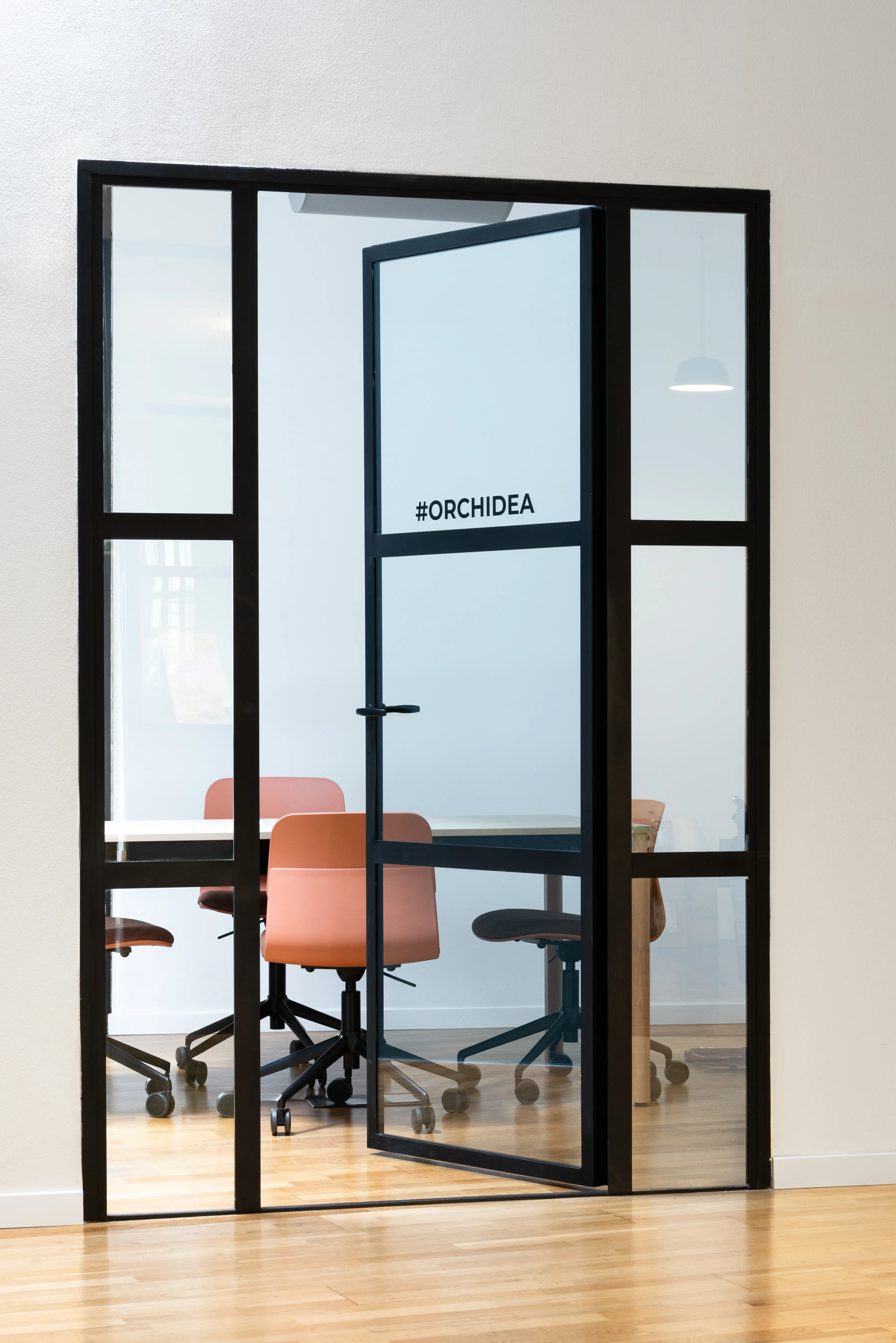 Salle de réunion vitrée Ogury à Milan, équipée de fauteuils terracotta et signalétique #Orchidea, réalisée par Slean.