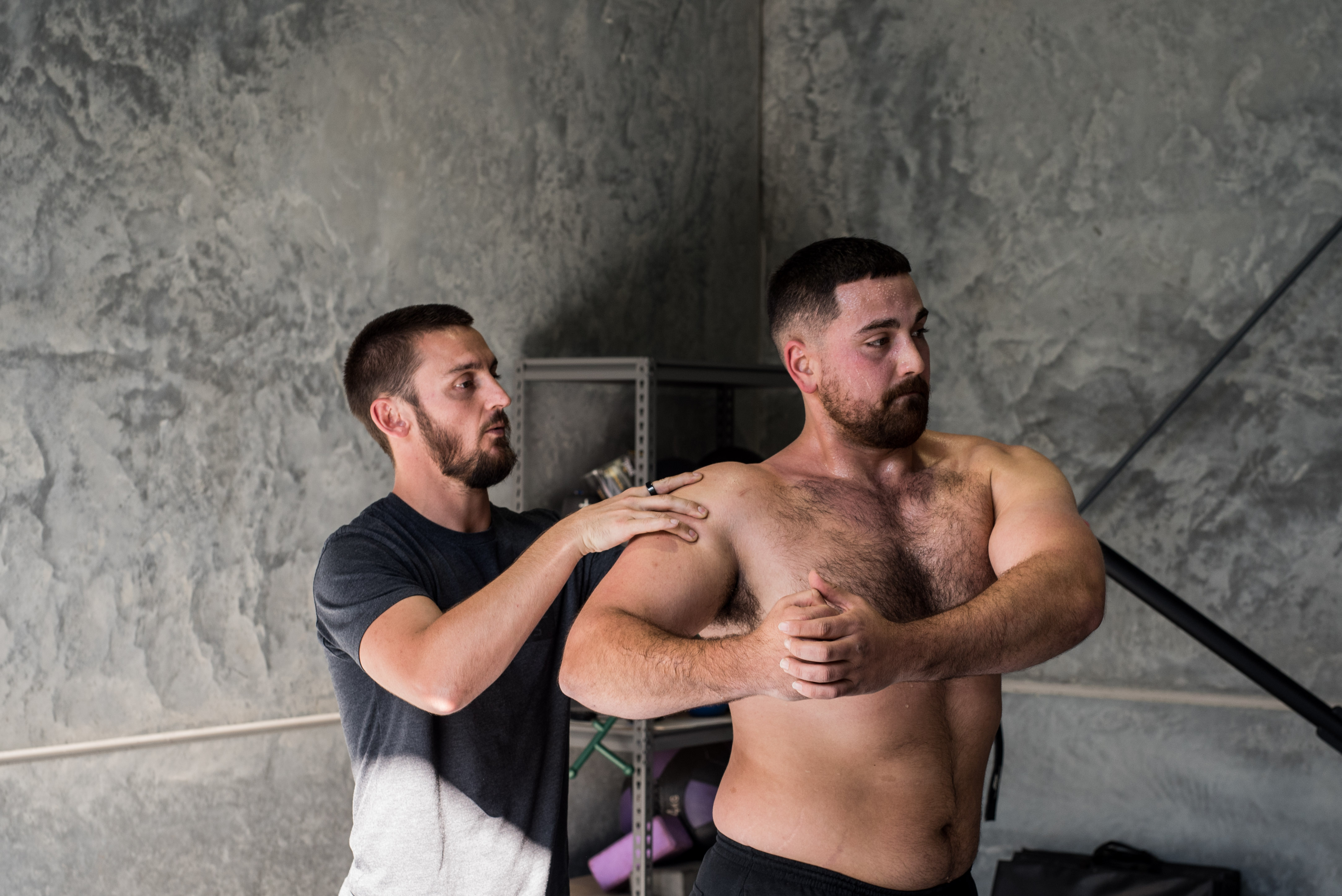 Trainer assists man stretching his shoulder in a gym.