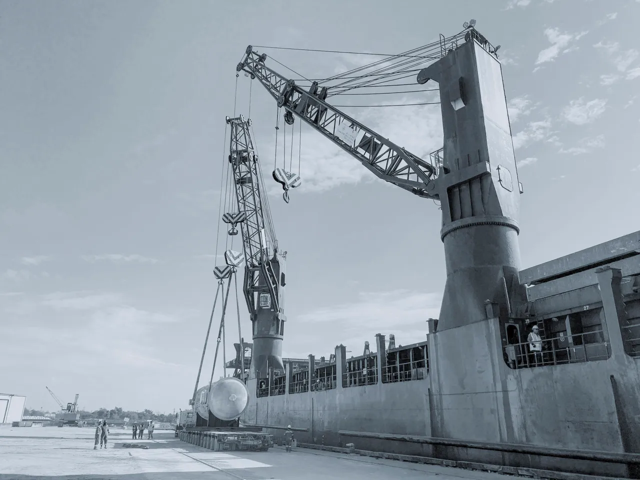 Intermodal project cargo transfer: Ship cranes discharging an industrial pressure vessel directly onto a specialized heavy-haul trailer at the port.