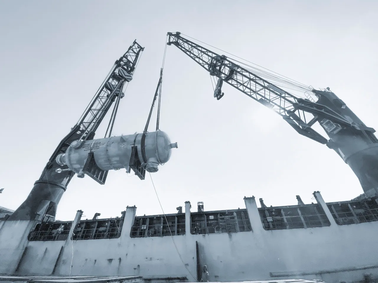Heavy-lift maritime engineering: Dual vessel cranes performing a tandem lift of an oversized industrial pressure vessel for global project cargo transport.