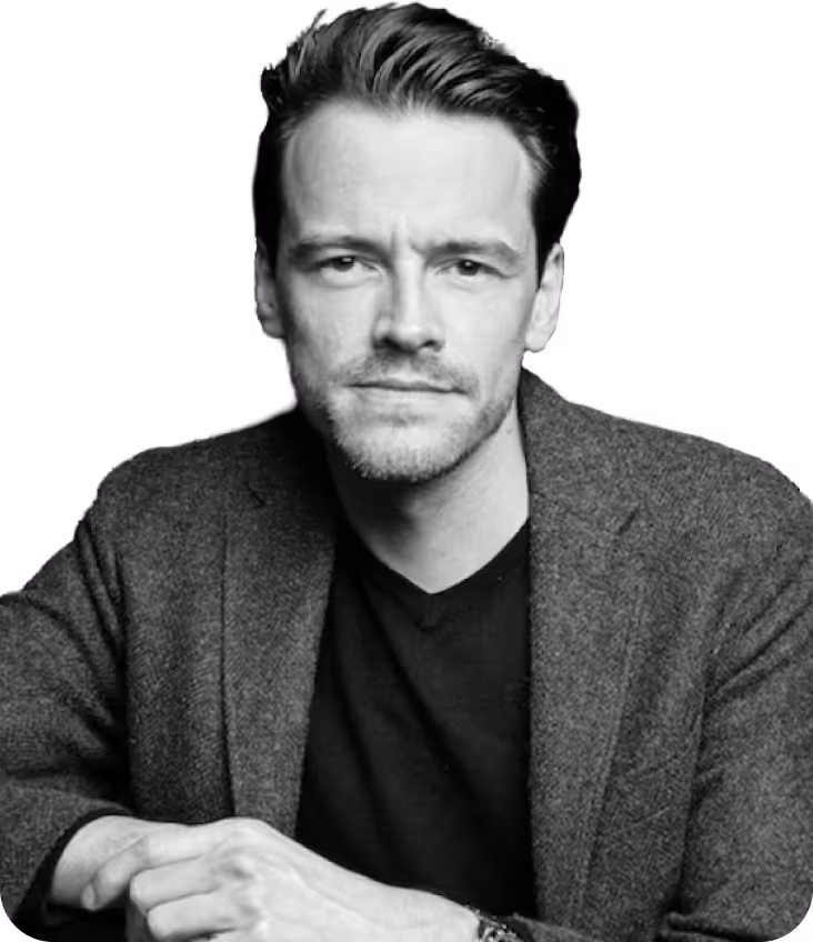 Black and white portrait of a man with neatly styled hair wearing a blazer and black shirt, looking directly at the camera.