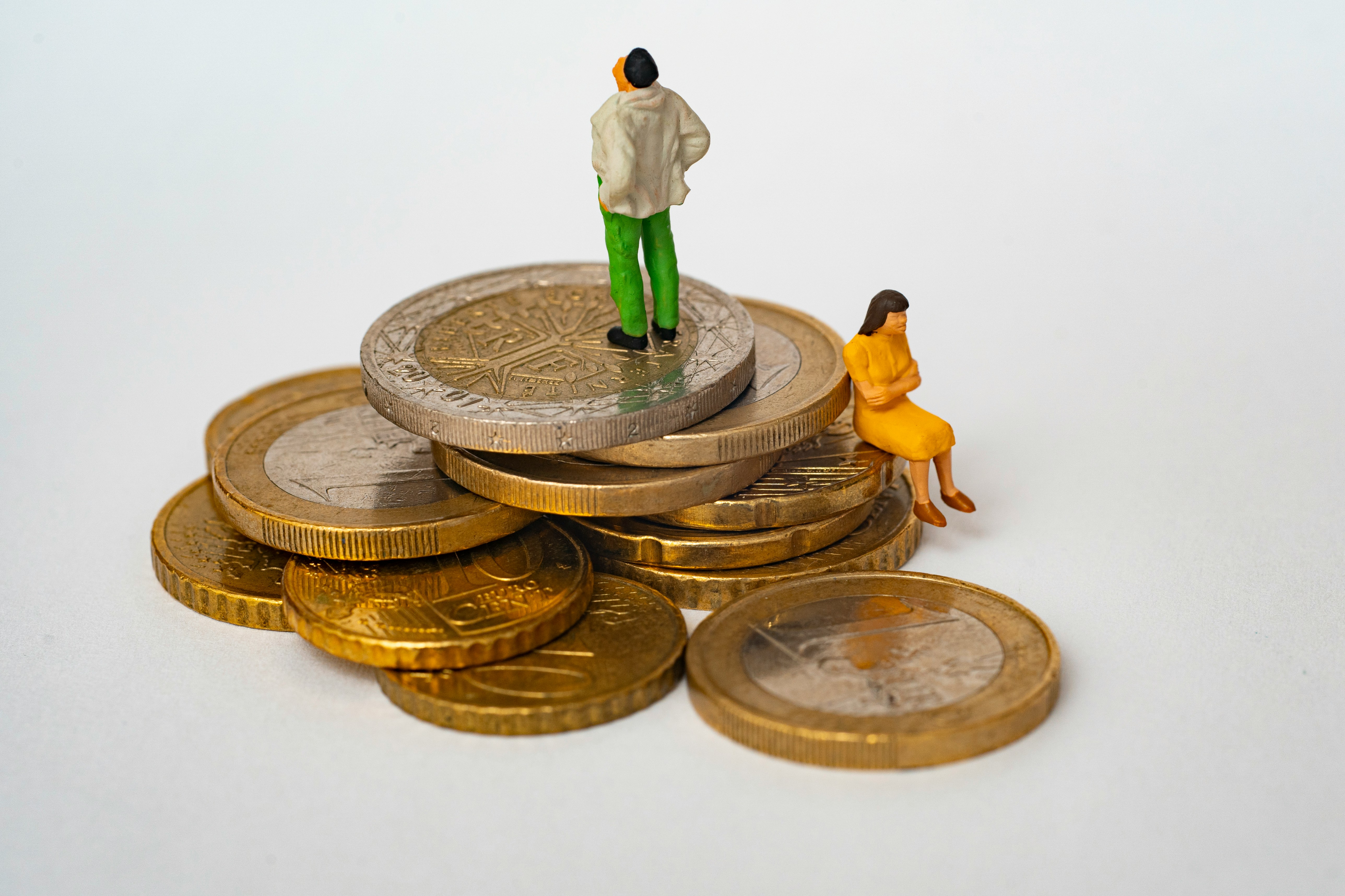 An arguing couple sit facing away from one another on a pile of coins.