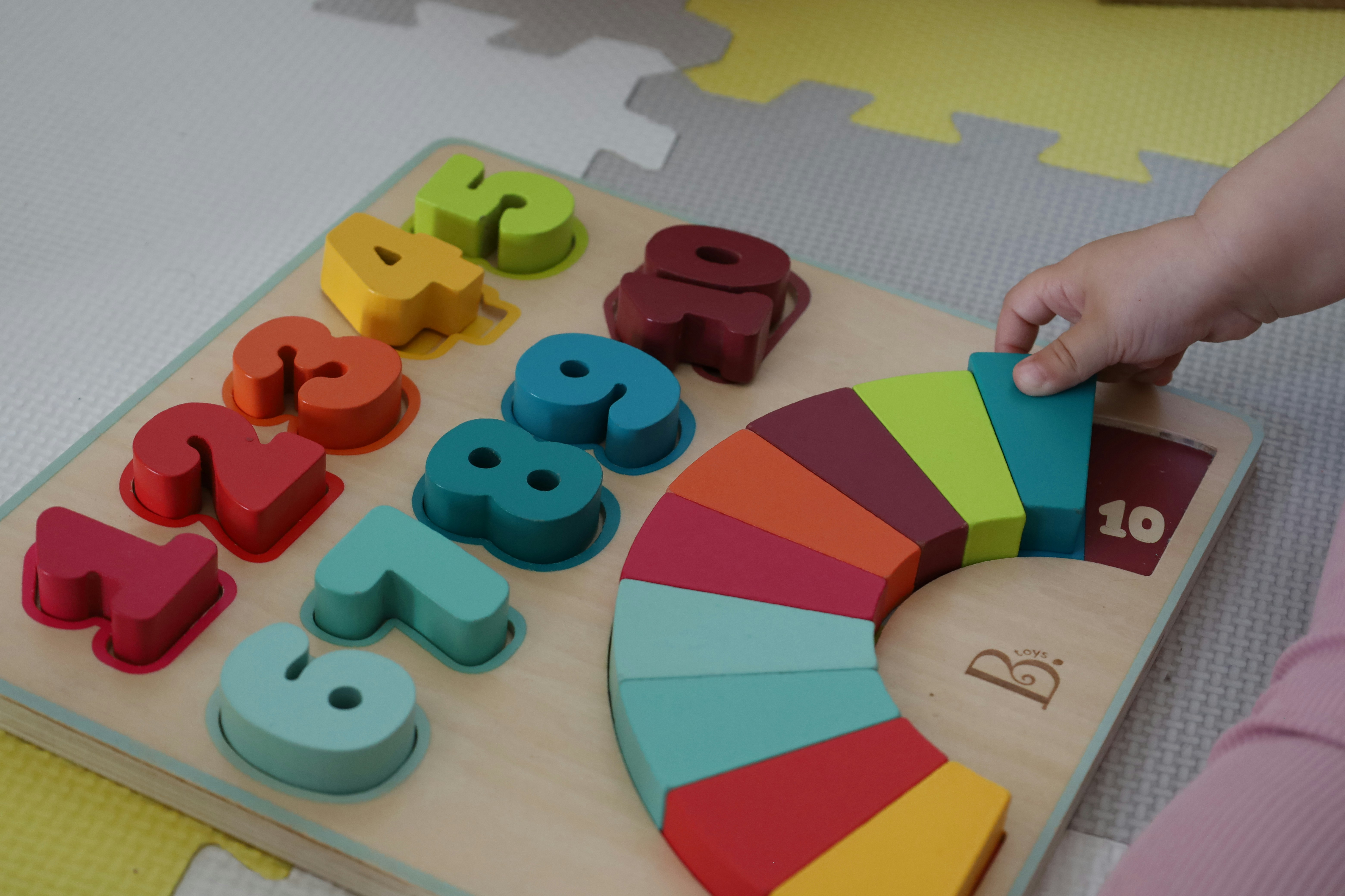 A baby's hand holding rainbow-coloured block toys.