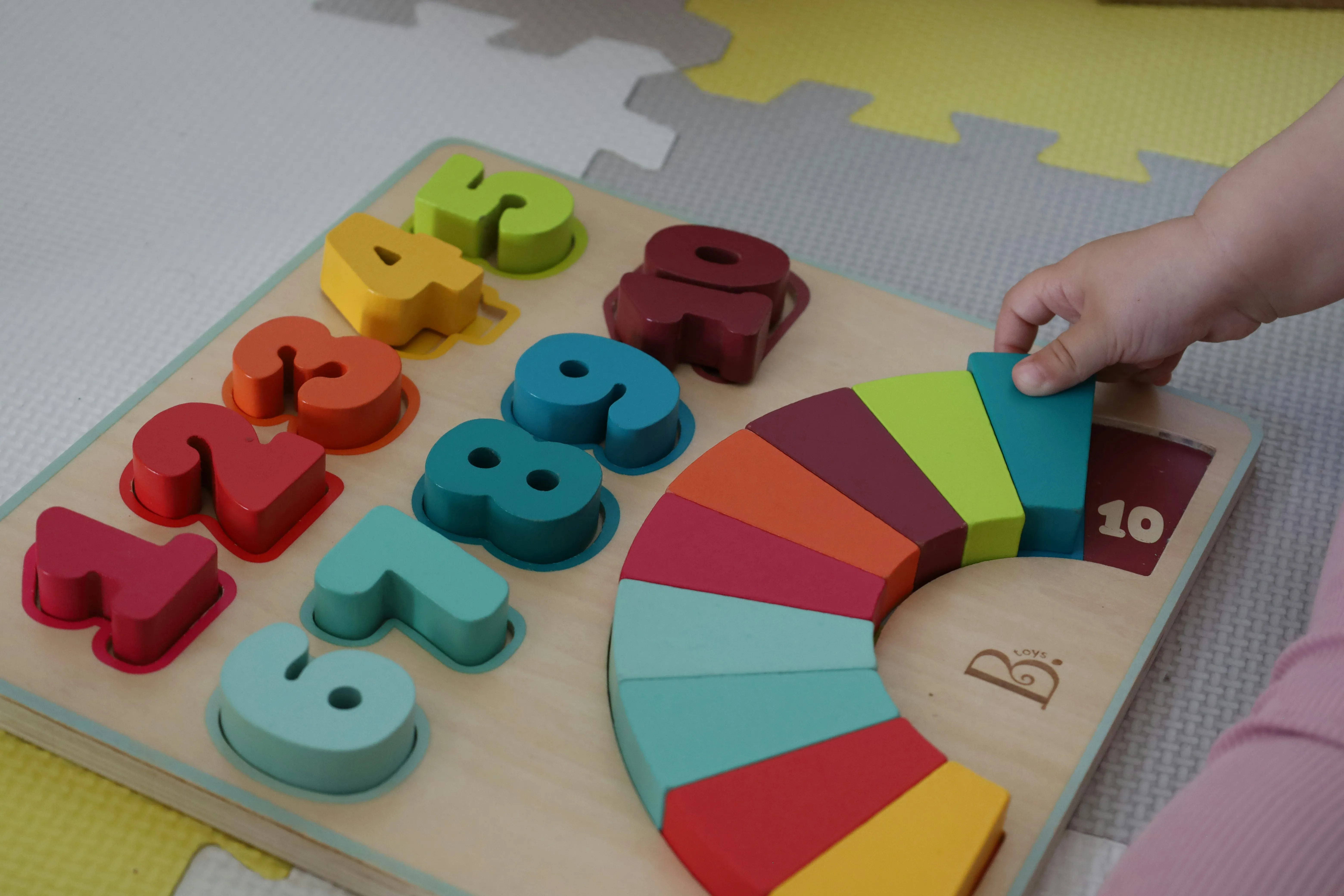 A baby's hand holding rainbow-coloured block toys.